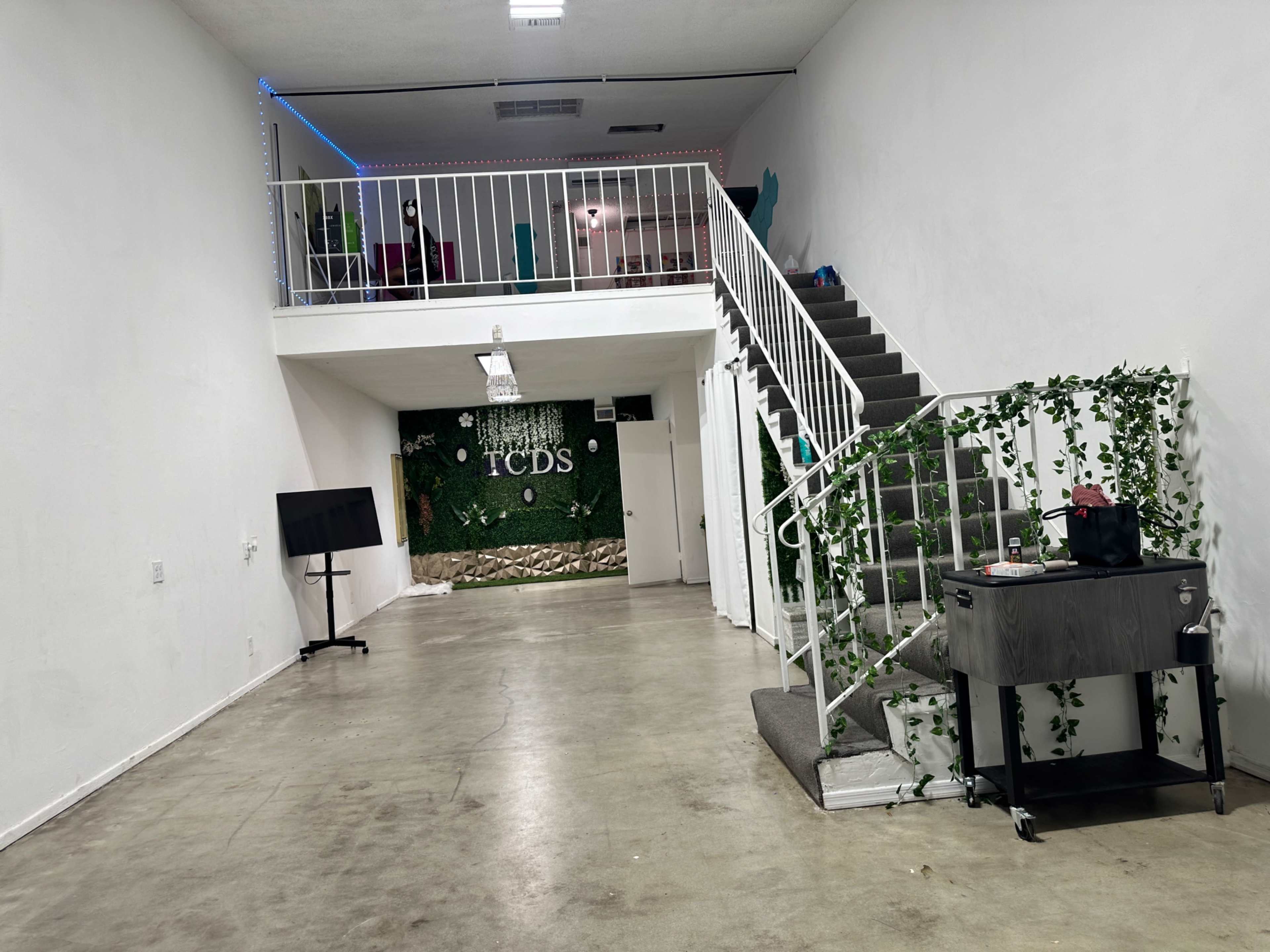 An interior space with a staircase leading to a second floor, a greenery-decorated wall, and minimal furniture.