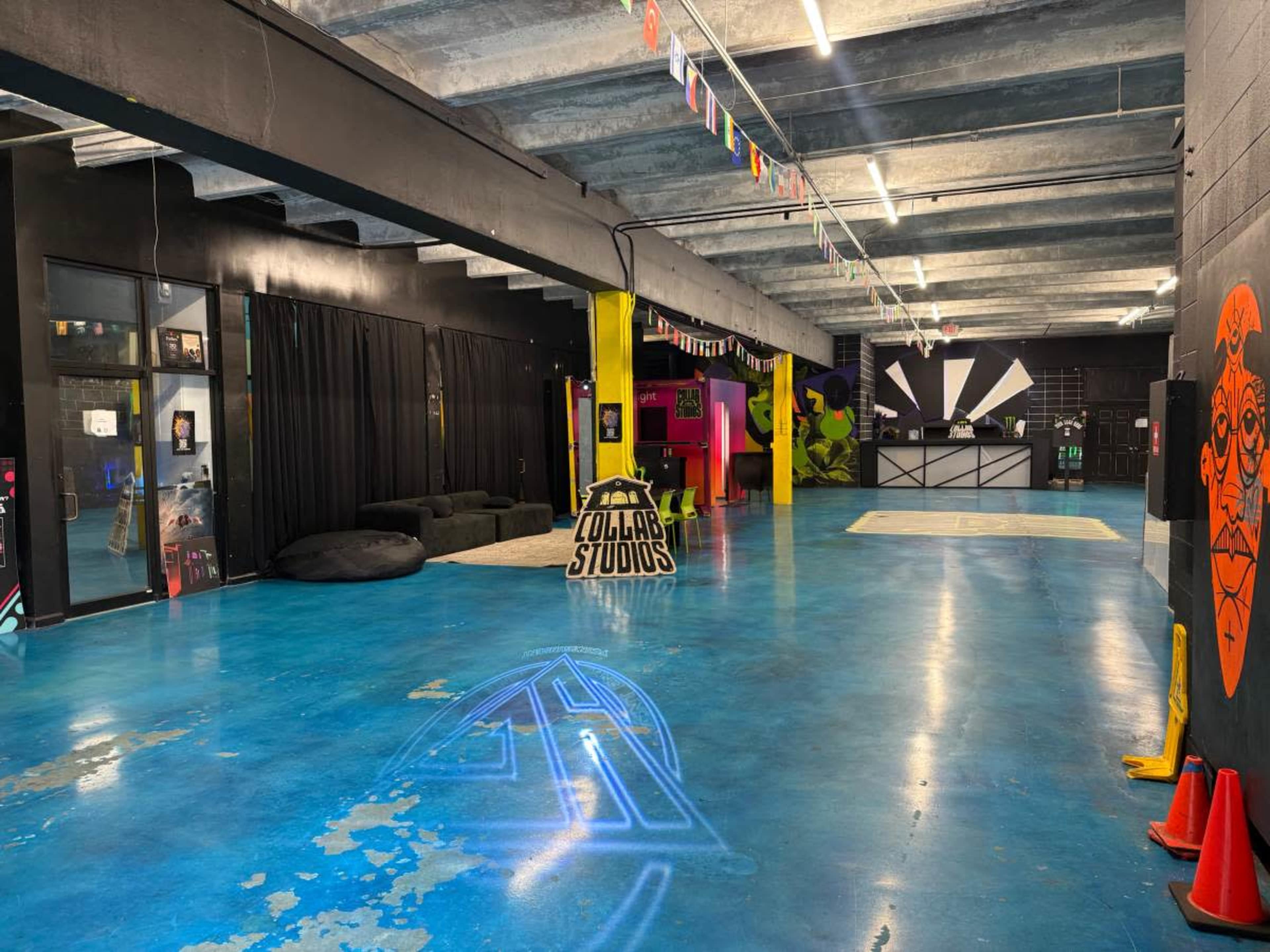 The image shows a spacious studio with a glossy blue floor, colorful walls, and various seating areas, illuminated by bright overhead lights.