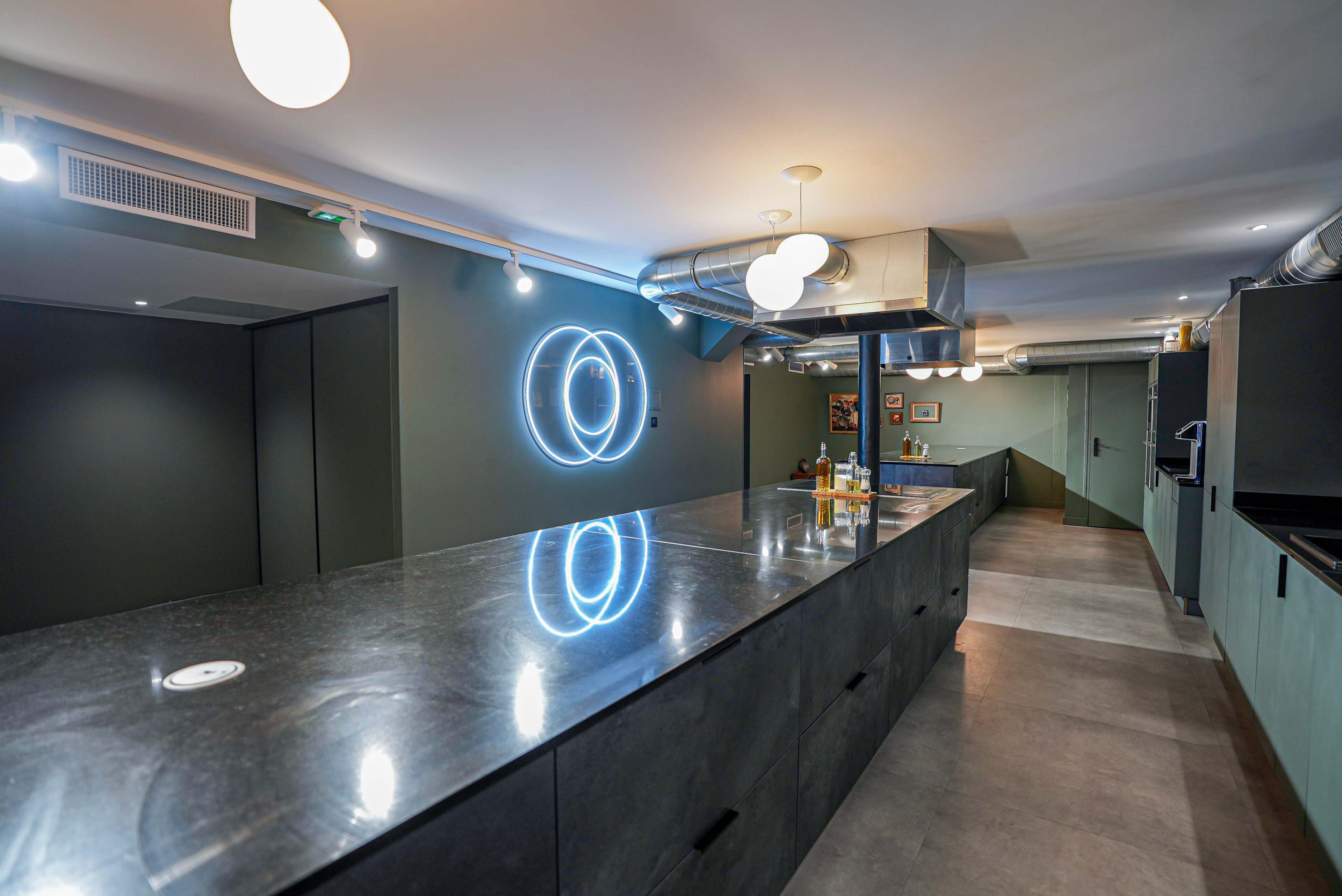 The image shows a modern kitchen with a sleek, dark countertop, illuminated by a circular neon light on the wall.