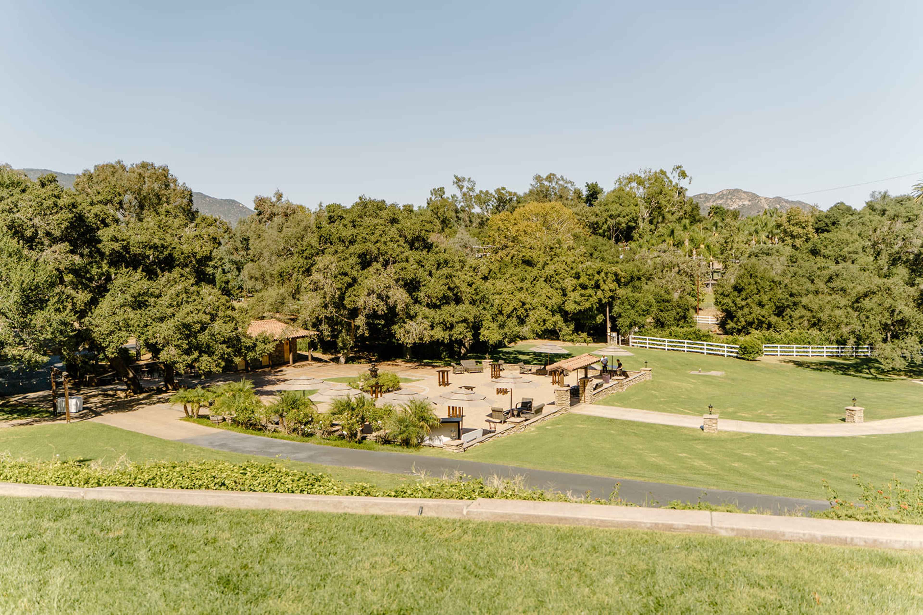 The image shows a large, open outdoor space surrounded by trees, featuring a flat area with benches and pathways.