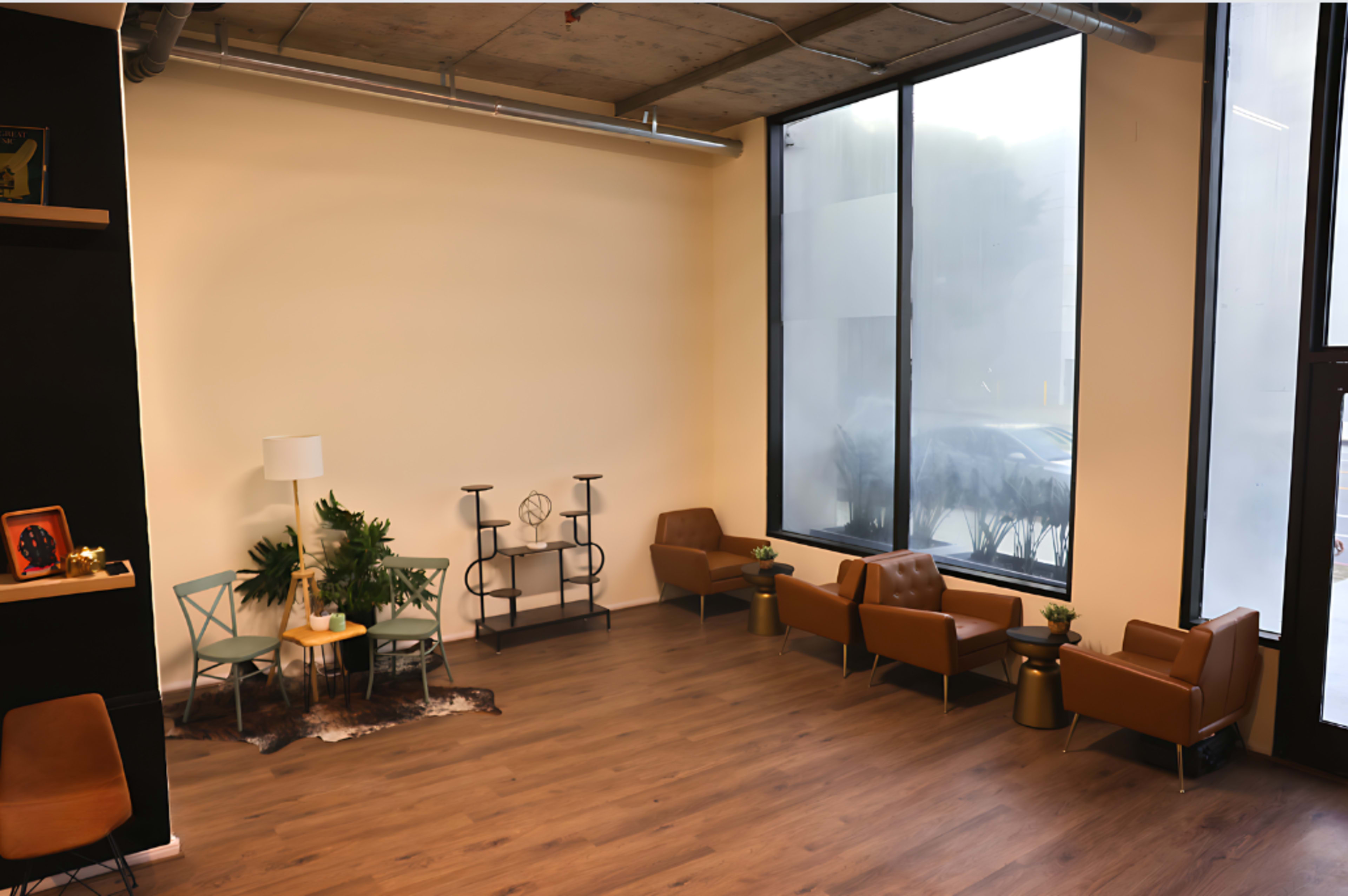 A modern indoor seating area with brown chairs, a small table, a potted plant, and large windows.
