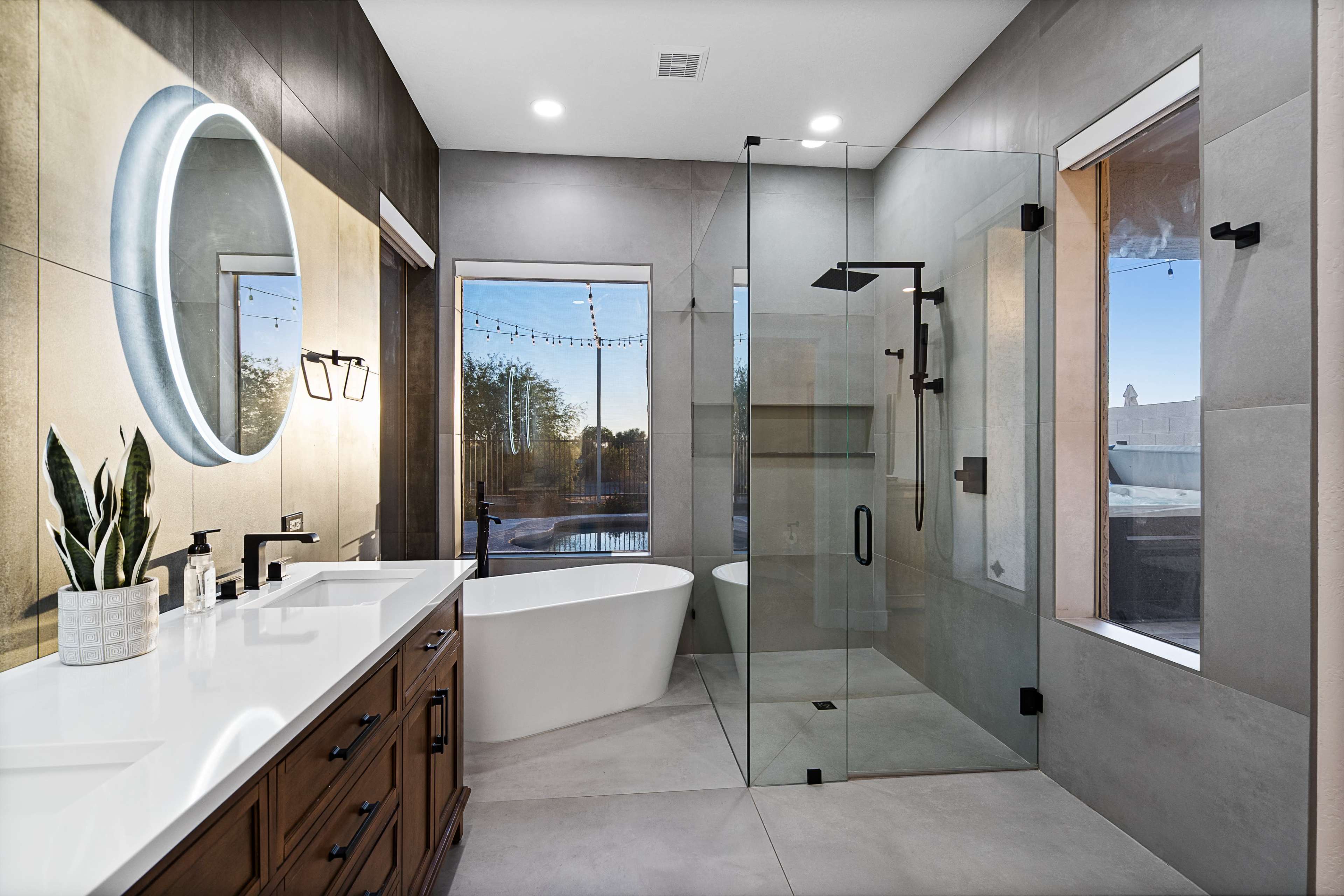 A modern bathroom featuring a freestanding bathtub, a glass shower enclosure, and a double vanity with a round mirror.
