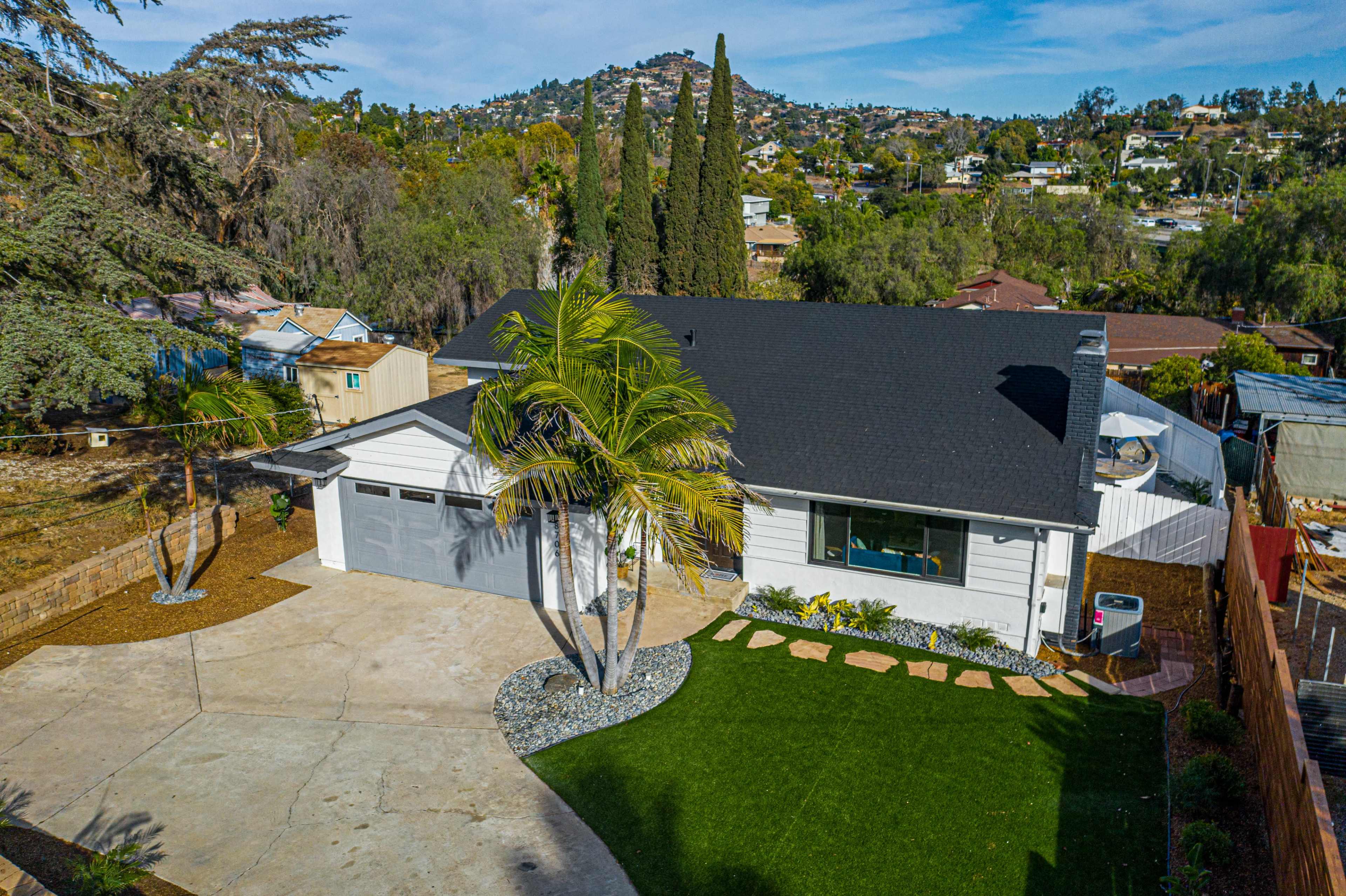 A single-story house with a gray garage sits next to a landscaped yard featuring a palm tree and a concrete driveway.