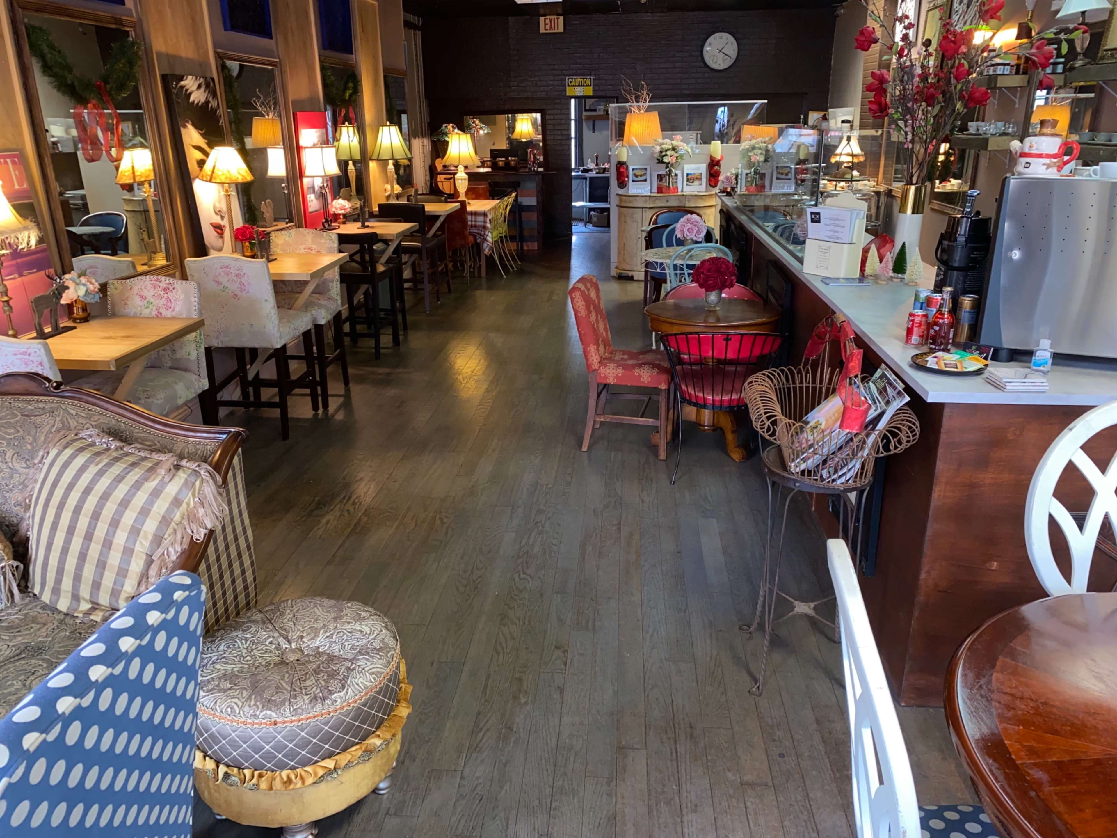 A cozy café interior with various tables, chairs, and lamps arranged along a wooden floor.