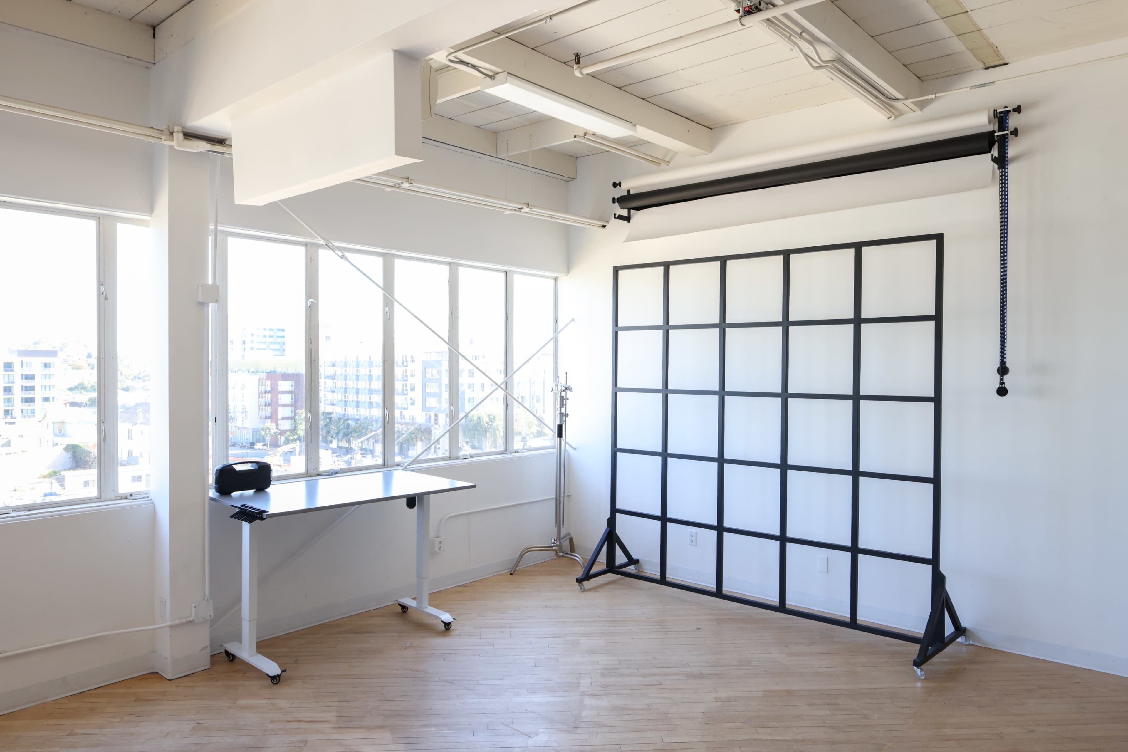 A bright, minimalist studio space featuring a desk and a backdrop setup against a large window.