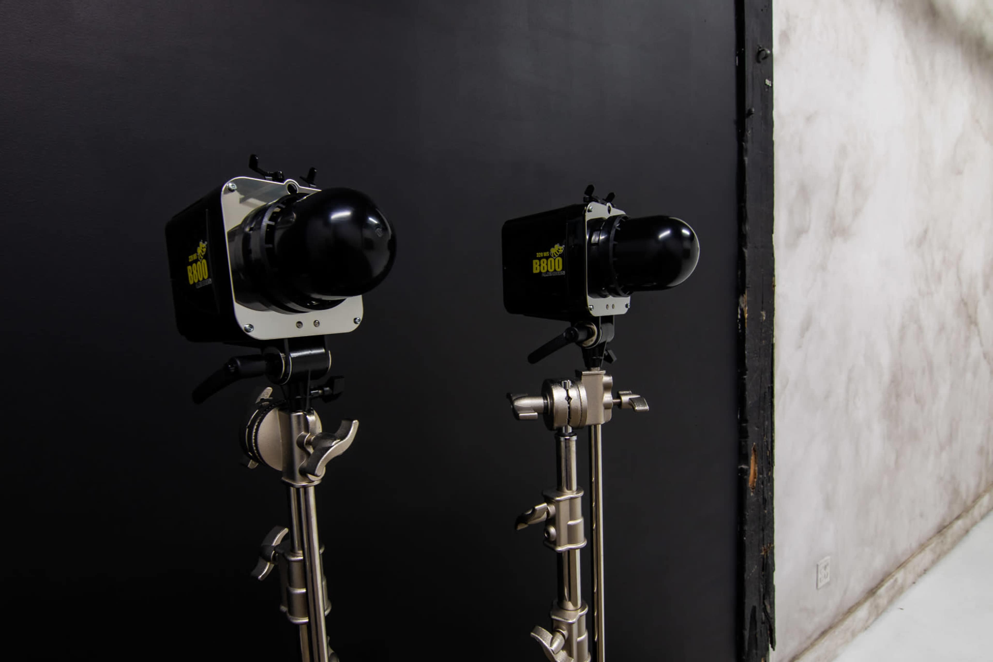 The image shows two studio lights mounted on silver stands against a dark textured wall.