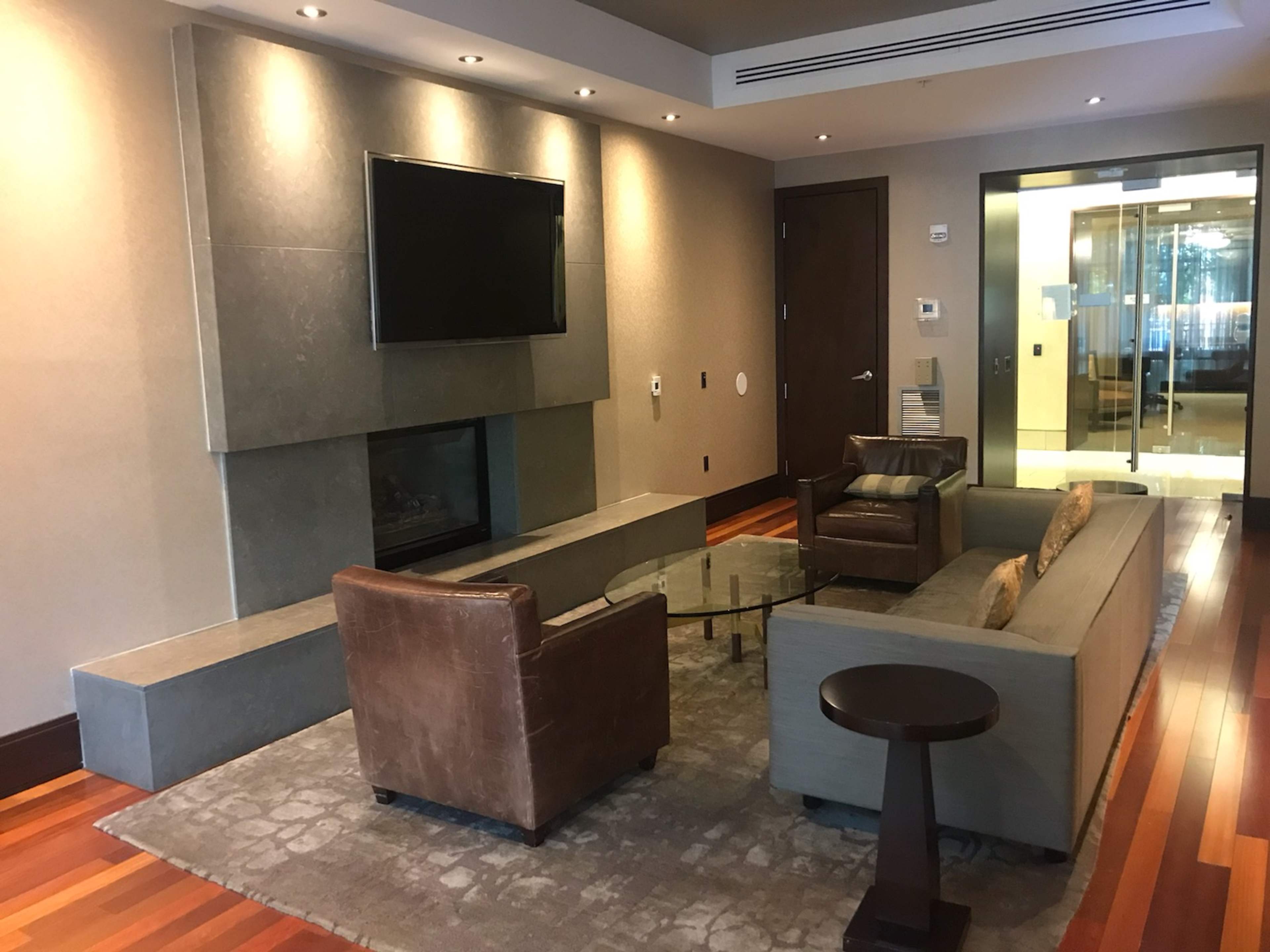 A modern living room with a sofa, two chairs, a coffee table, a wall-mounted television, and a fireplace, all set against a backdrop of wooden flooring and stylish neutral walls.