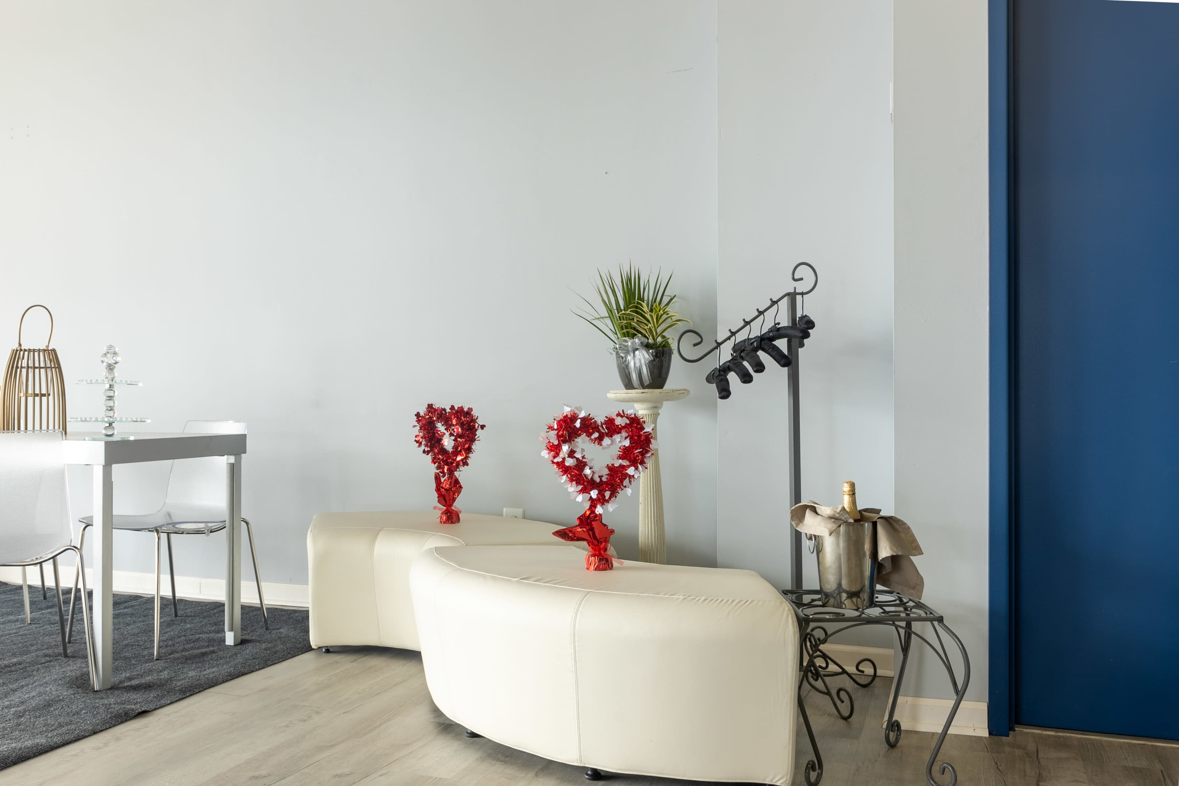 A modern interior with two heart-shaped decorations on a curved white bench, a dining area with a table, and a blue door in the background.