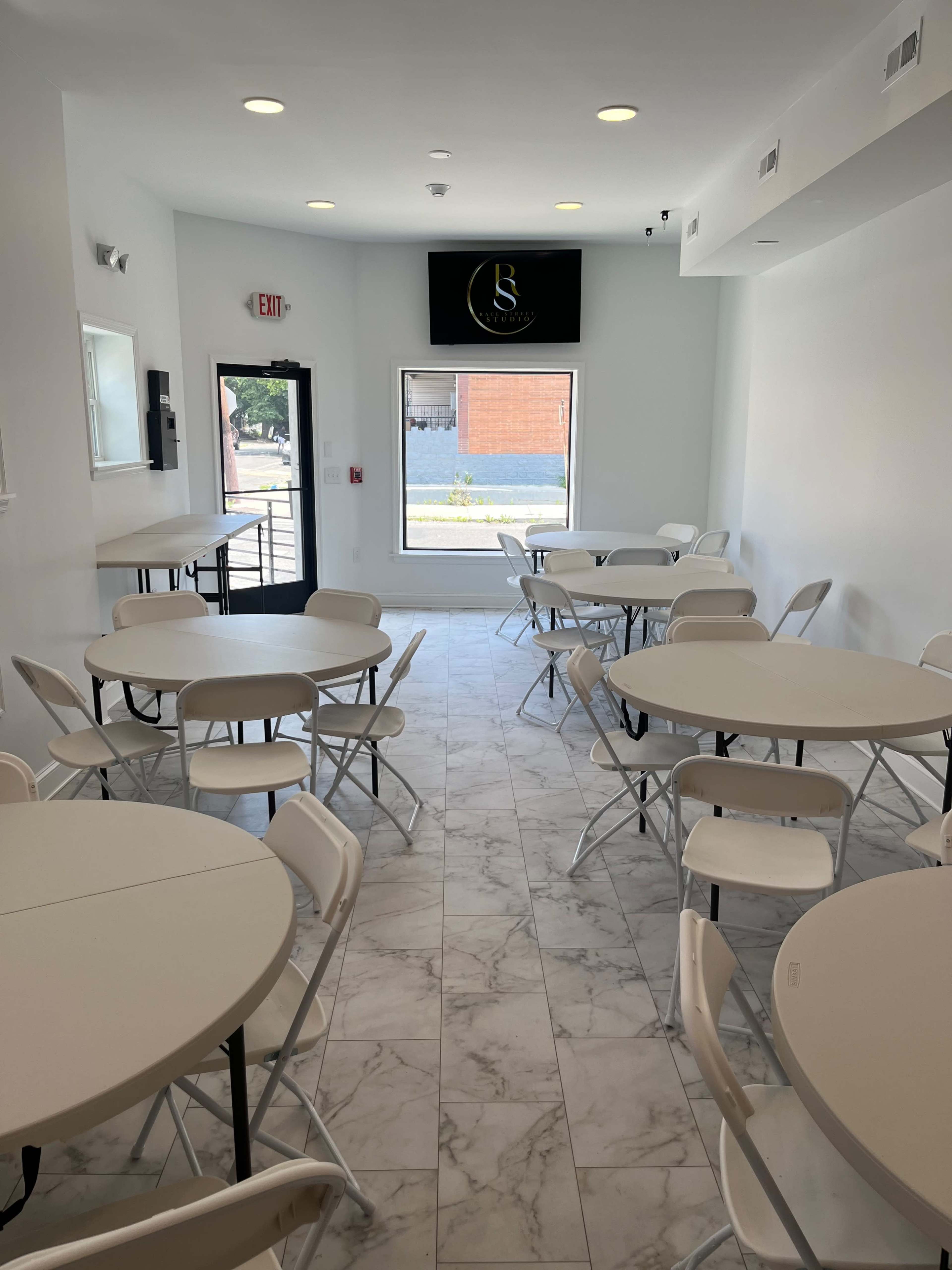 The image shows a bright, modern dining area with several round tables and chairs arranged throughout the space.