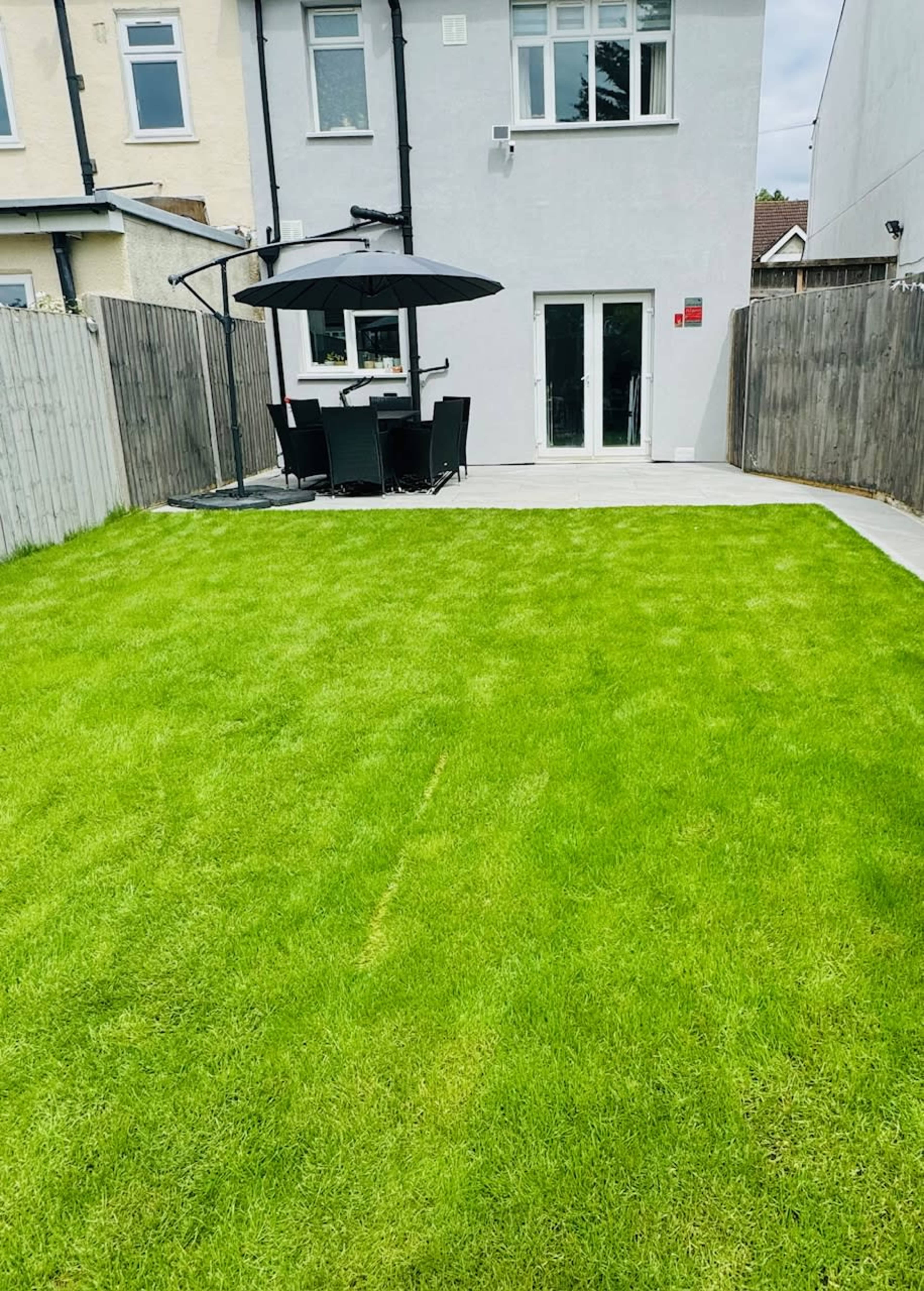 A well-maintained green lawn in a backyard with a patio area containing a dining table and a large umbrella.