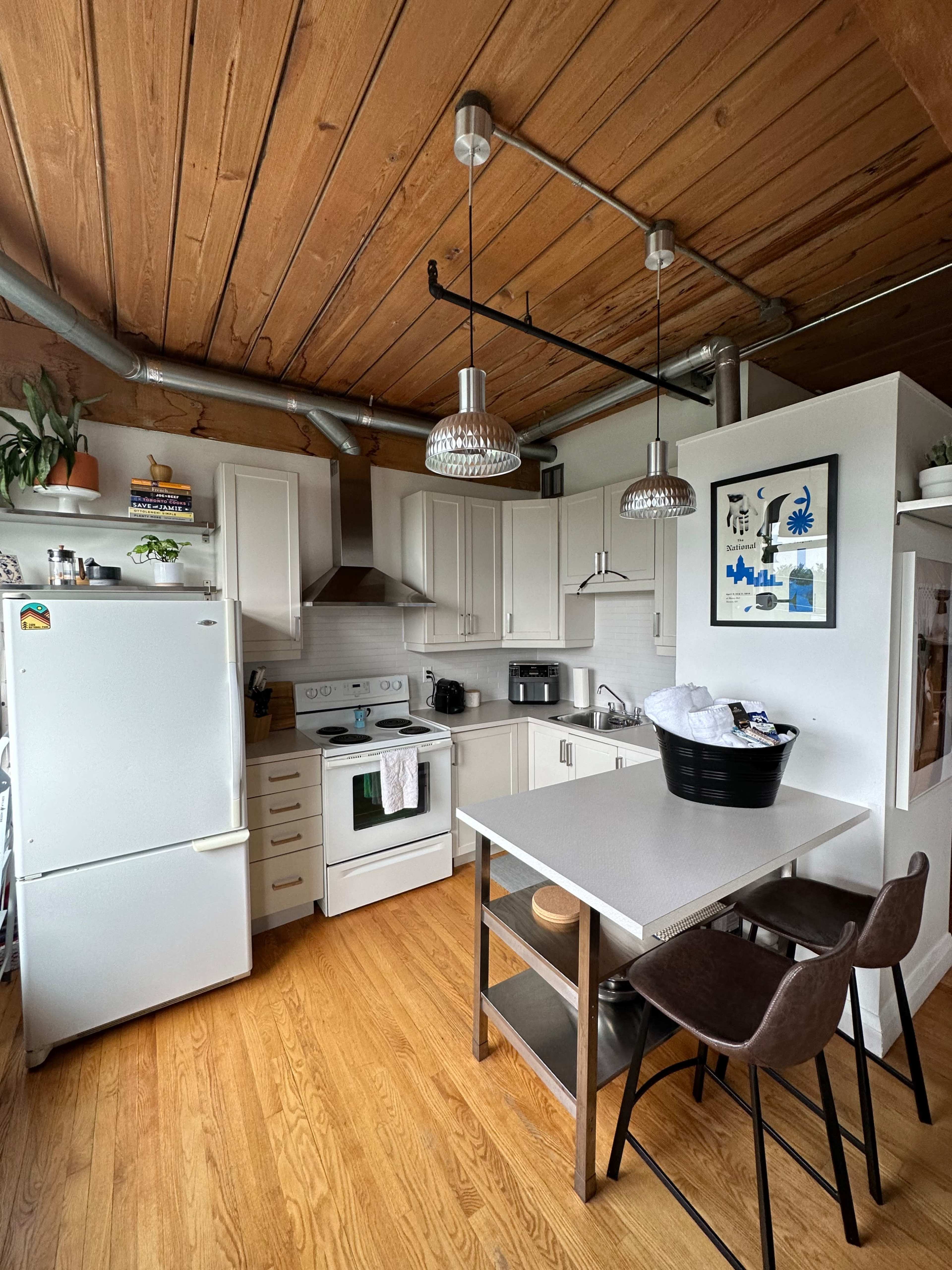 A modern kitchen features white cabinetry, stainless steel appliances, a central island, and wooden flooring.
