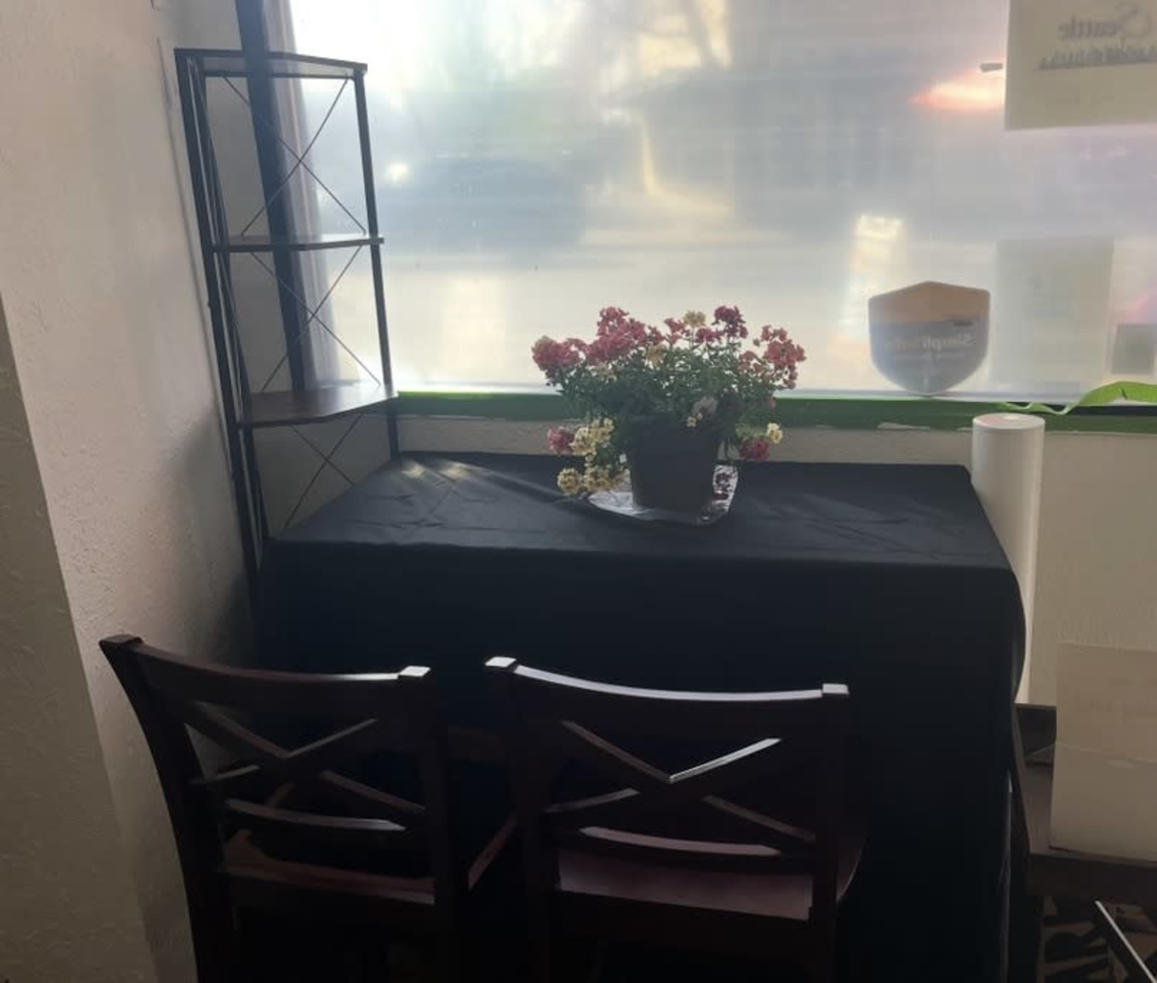 A small table covered with a black cloth is set against a window, adorned with a potted plant and two wooden chairs on either side.