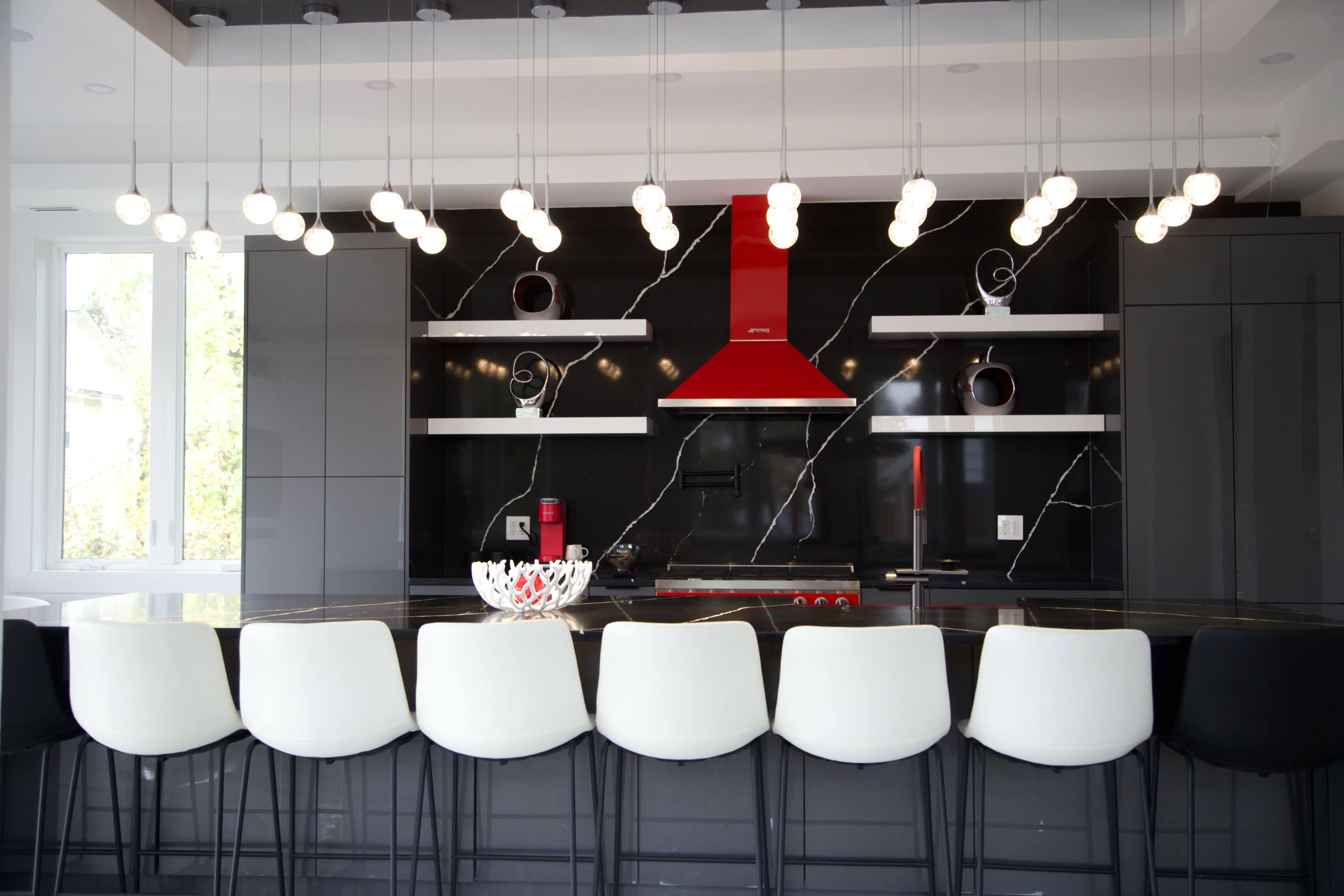 The image shows a modern kitchen with a black and white color scheme, featuring a sleek island with white bar stools and bright pendant lights hanging above.