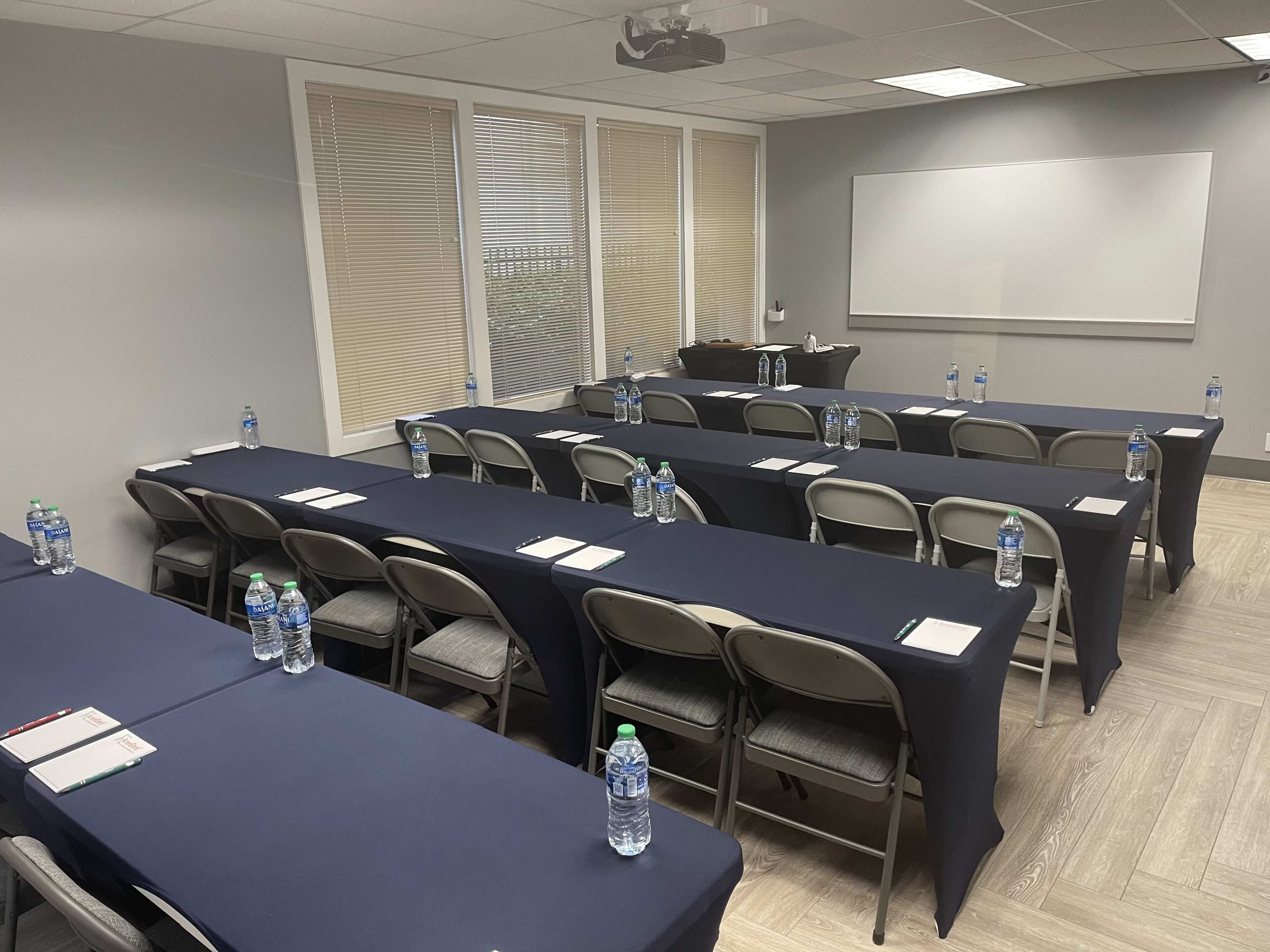 A conference room is set up with two rows of tables covered in dark cloth, each with water bottles and notepads arranged neatly.