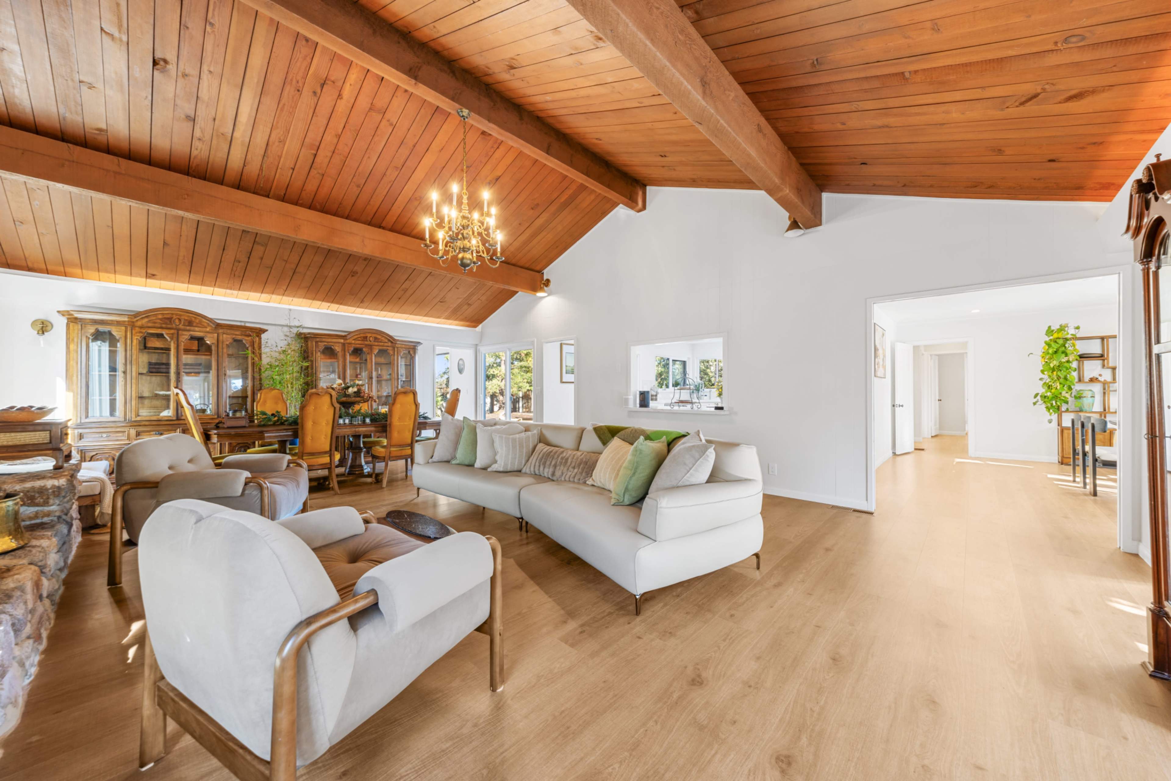 The image shows a spacious living area with a high wooden-beamed ceiling, a large white sofa, and a dining set in the background.
