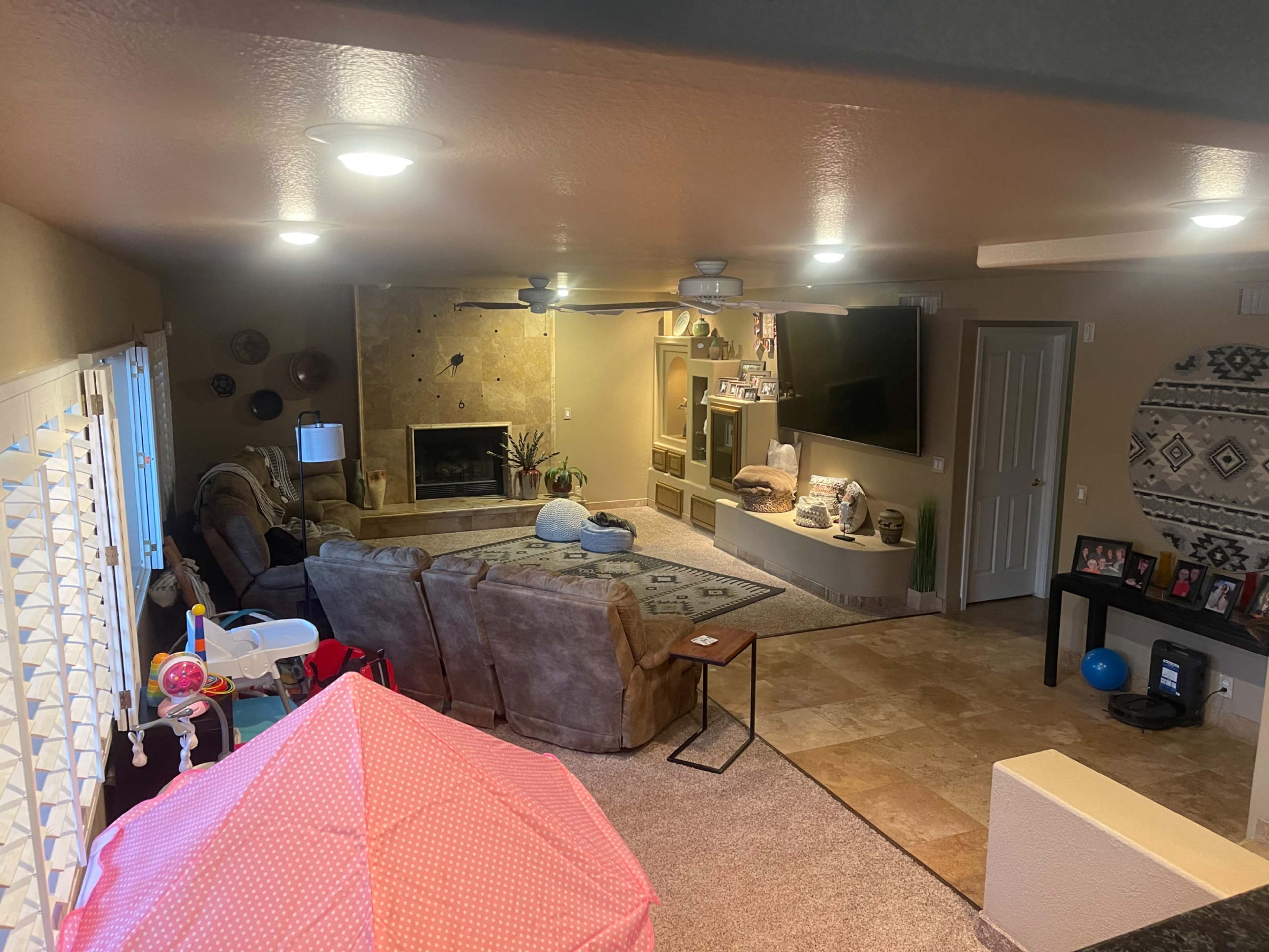 A living room features a beige couch, a fireplace, a television mounted on the wall, and various decorative elements throughout.