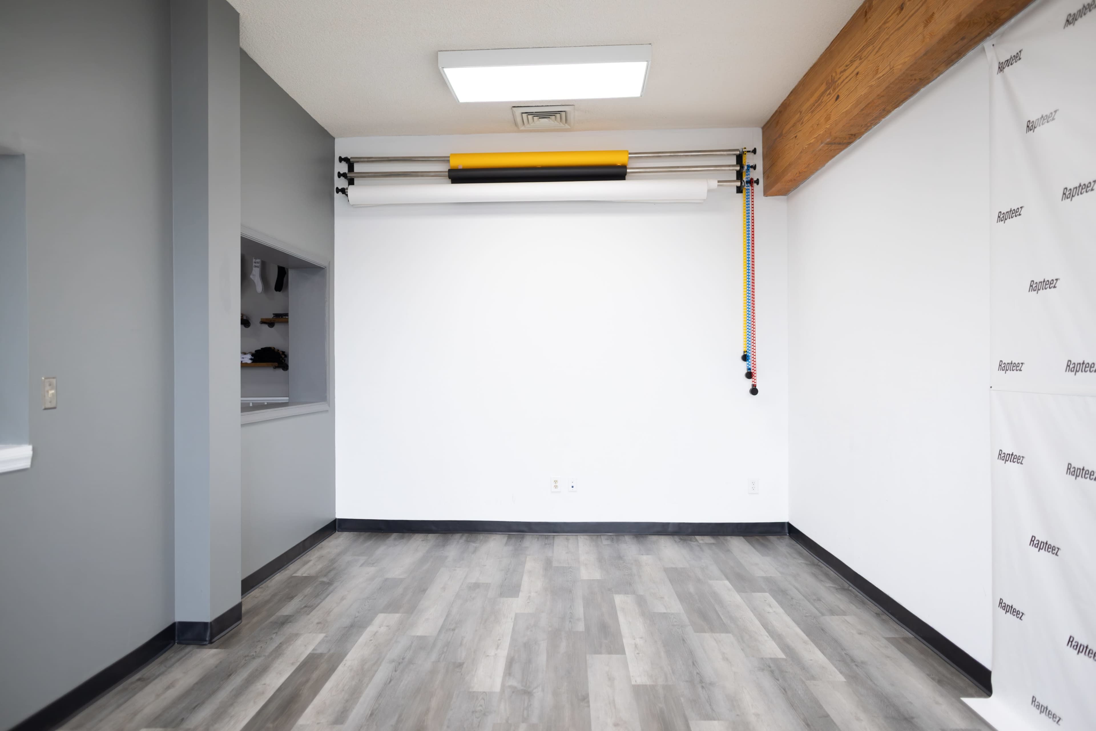 The image shows a spacious room with gray and white walls, a wooden beam overhead, and a backdrop setup along one wall.