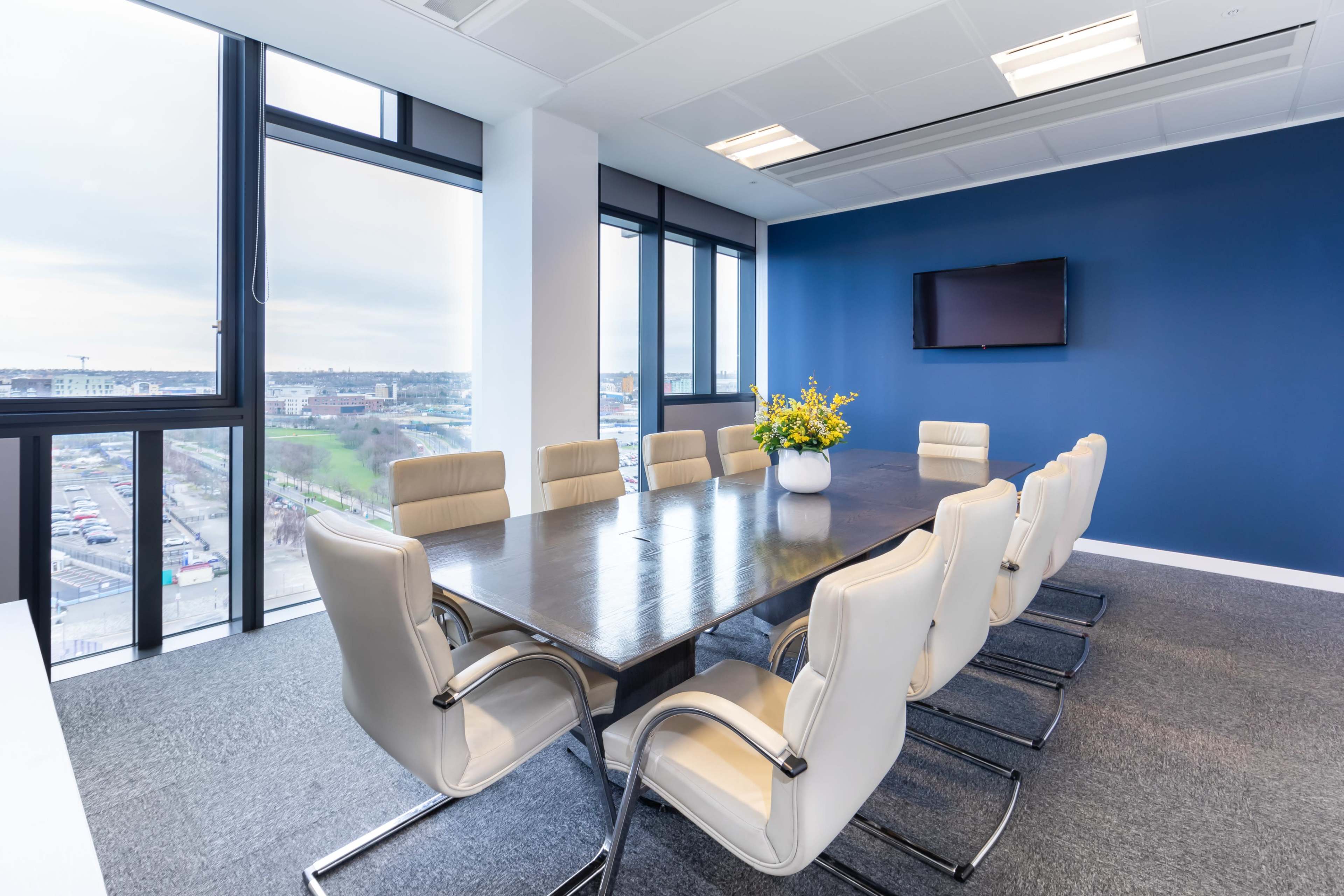 A large, modern conference room features a long table surrounded by white leather chairs, with a window showcasing a view of the outside landscape.