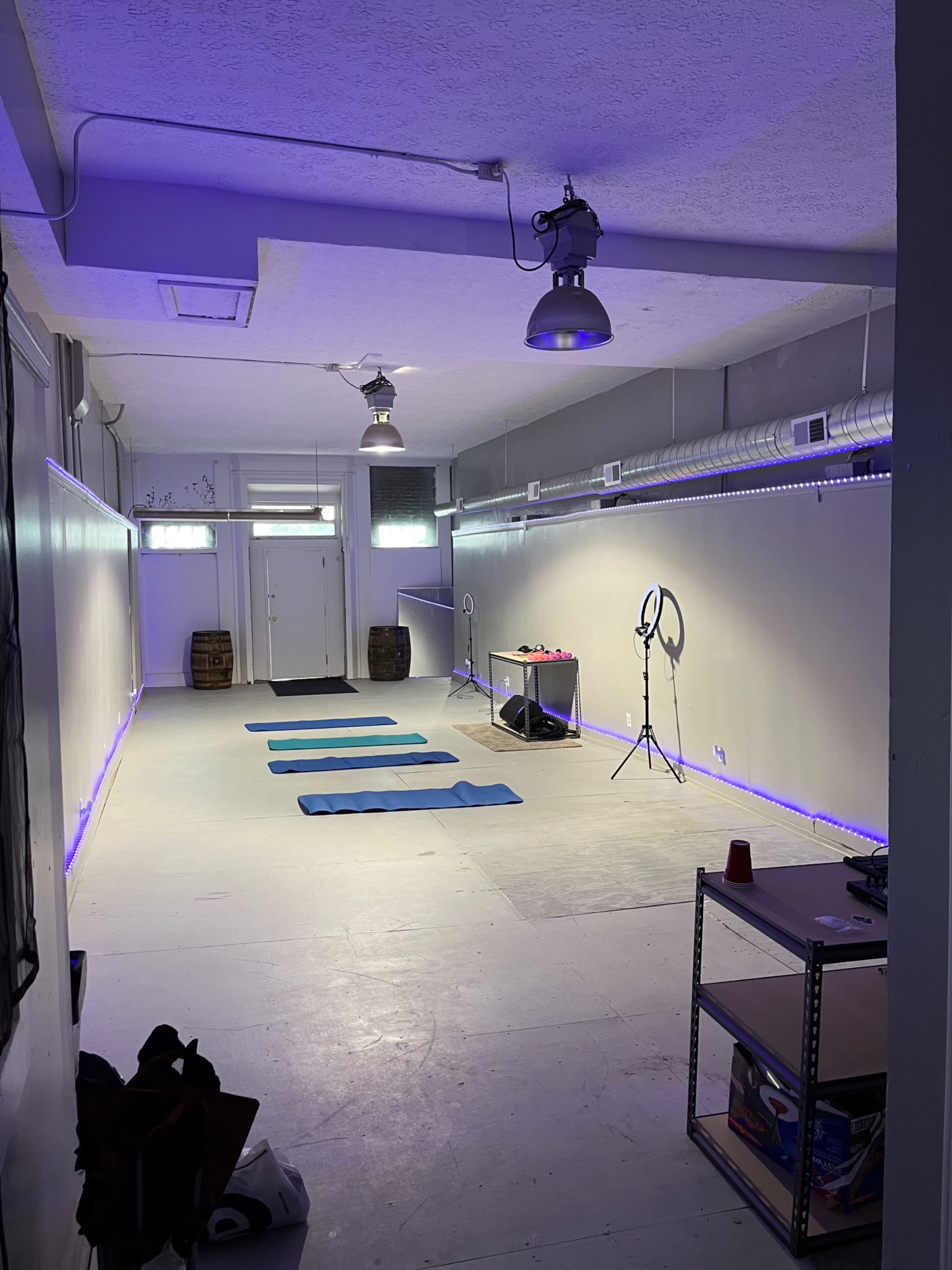 A spacious yoga studio with blue exercise mats arranged on the floor and illuminated by purple LED lights.