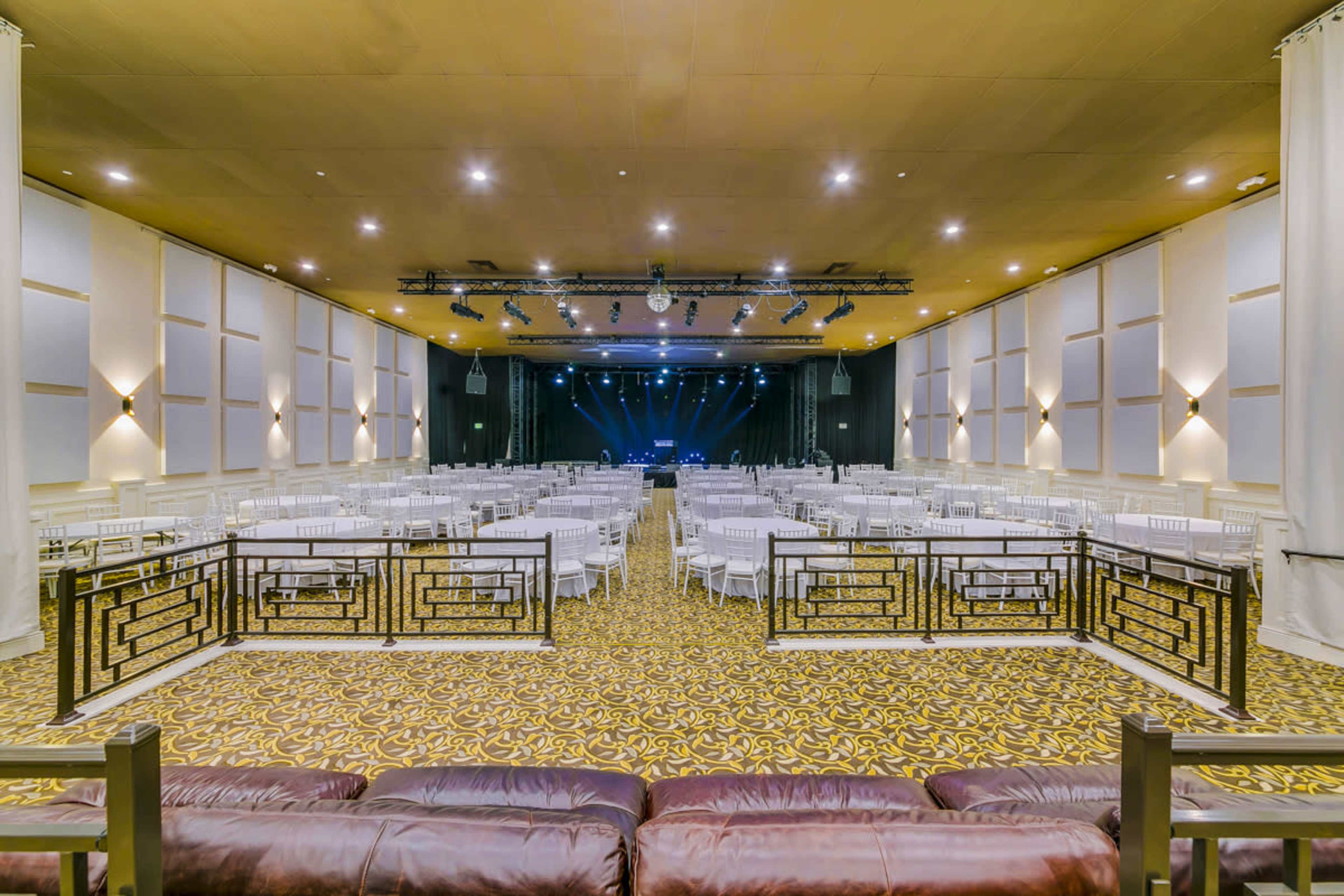 A spacious event hall set up with rows of white chairs and a stage featuring stage lights in the background.