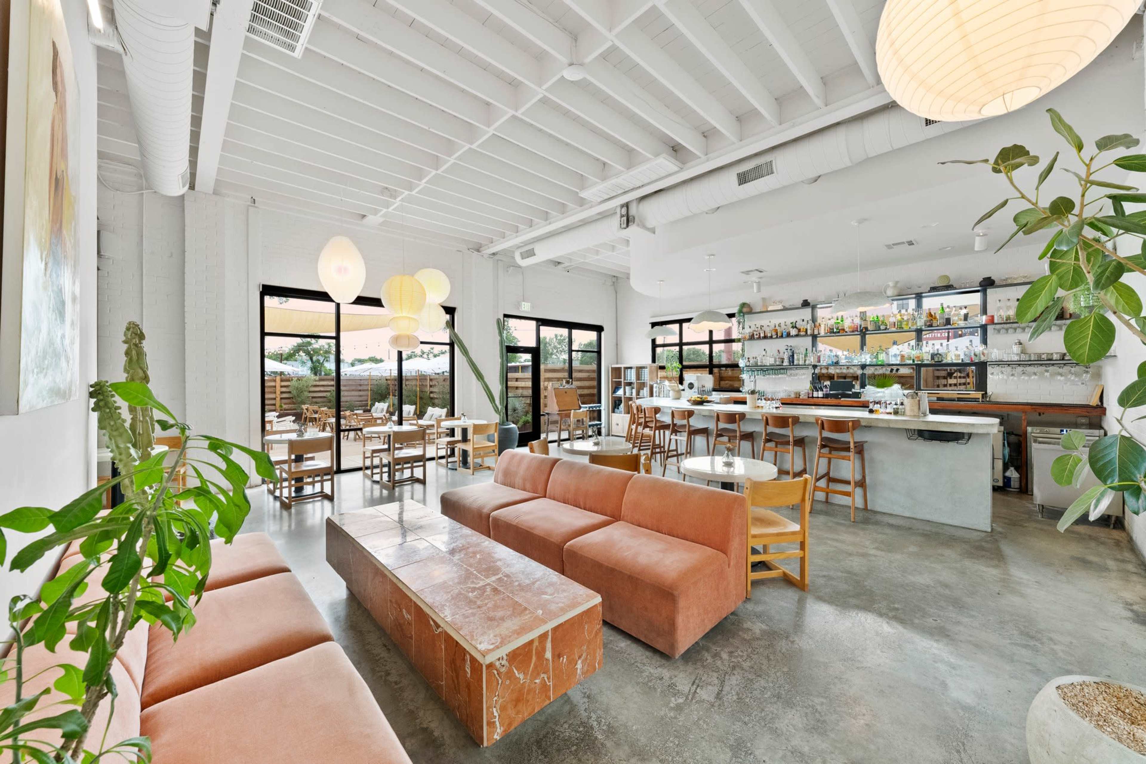 The image shows a modern café interior with a peach-colored couch, wooden furniture, and a bar area with shelves displaying various beverages.