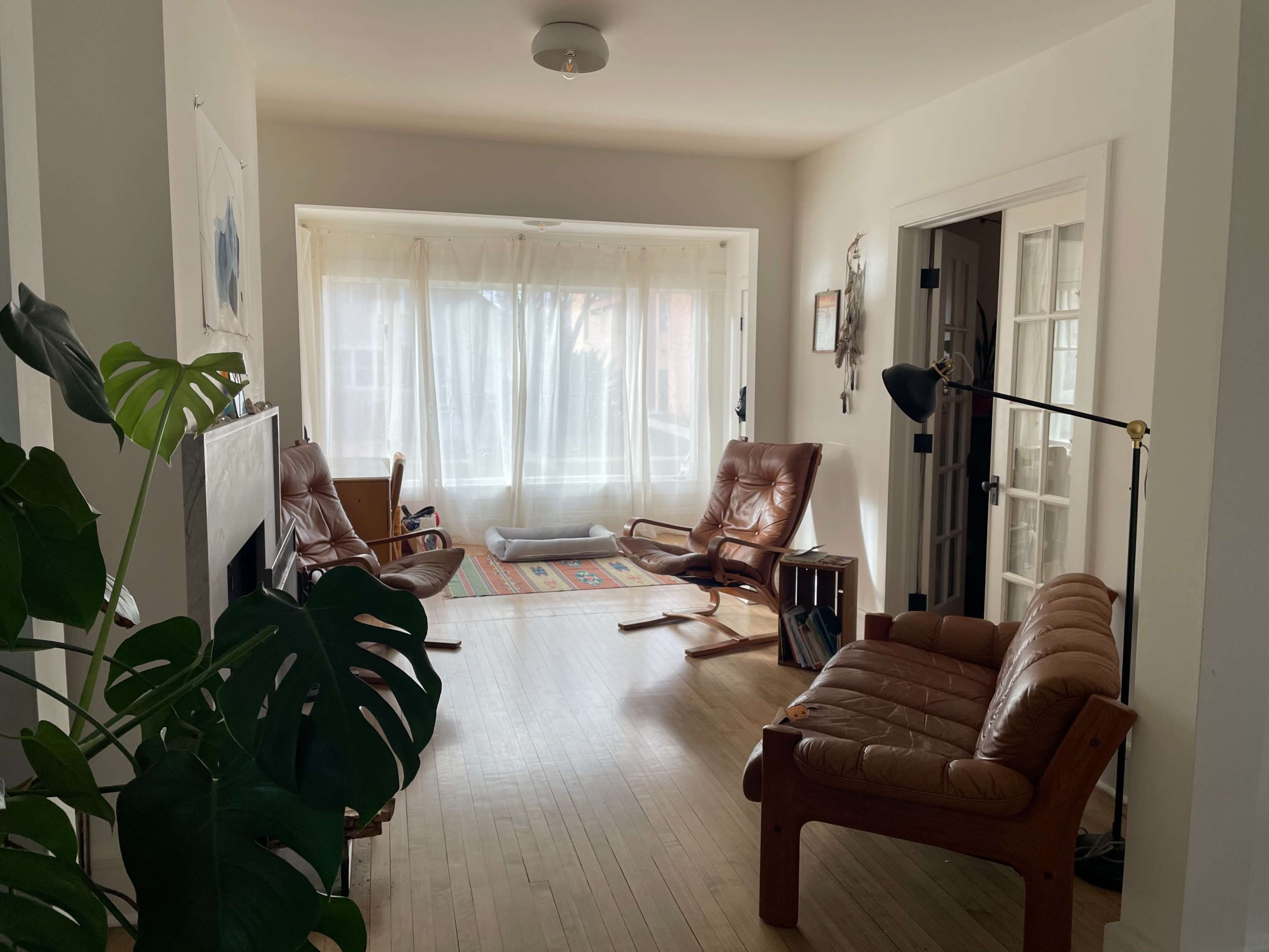 A bright, open living room with two leather chairs, a small table, and large windows covered with sheer curtains.