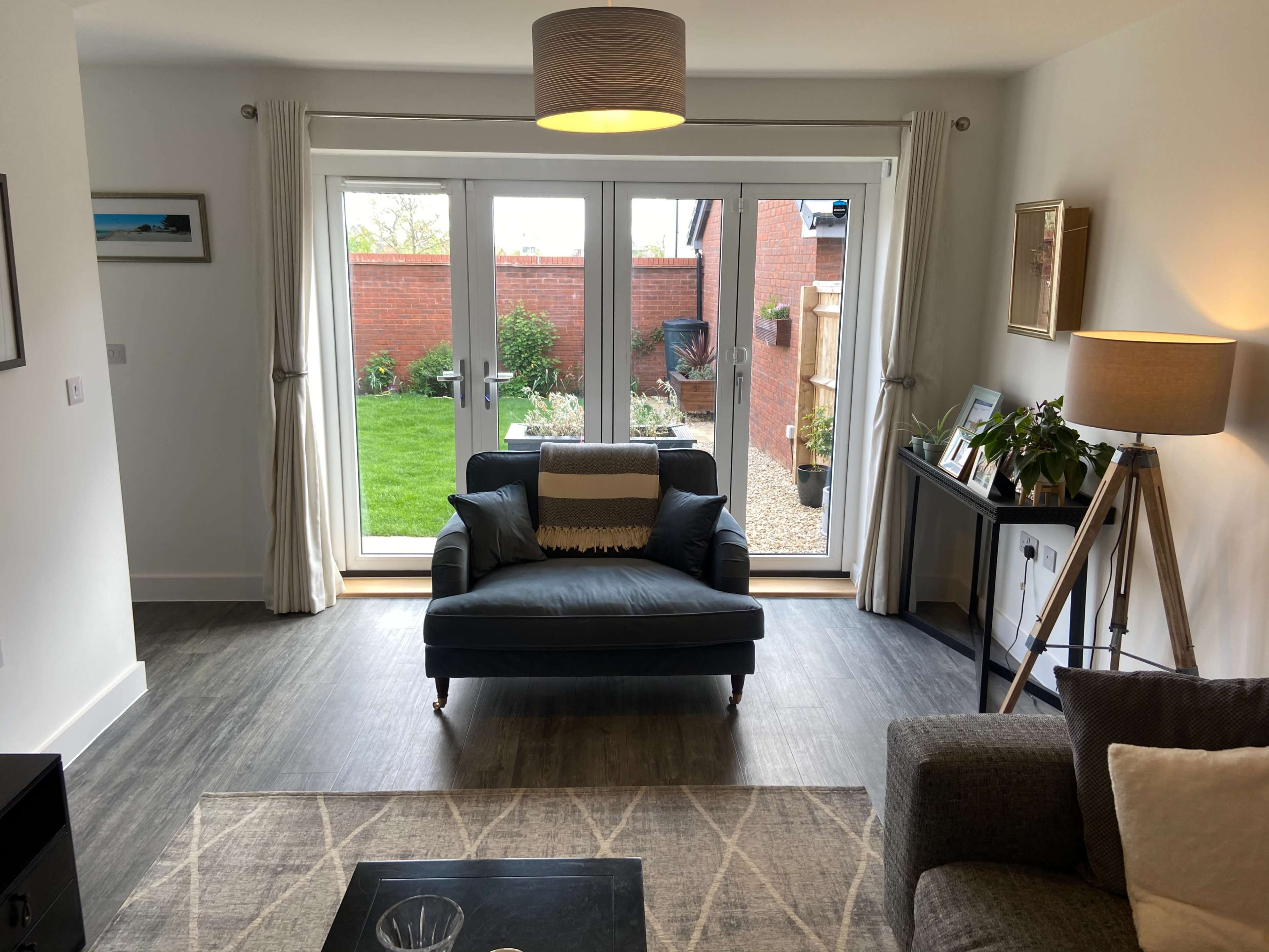 A living room features a blue armchair, a gray sofa, and large glass doors that open to a garden area.
