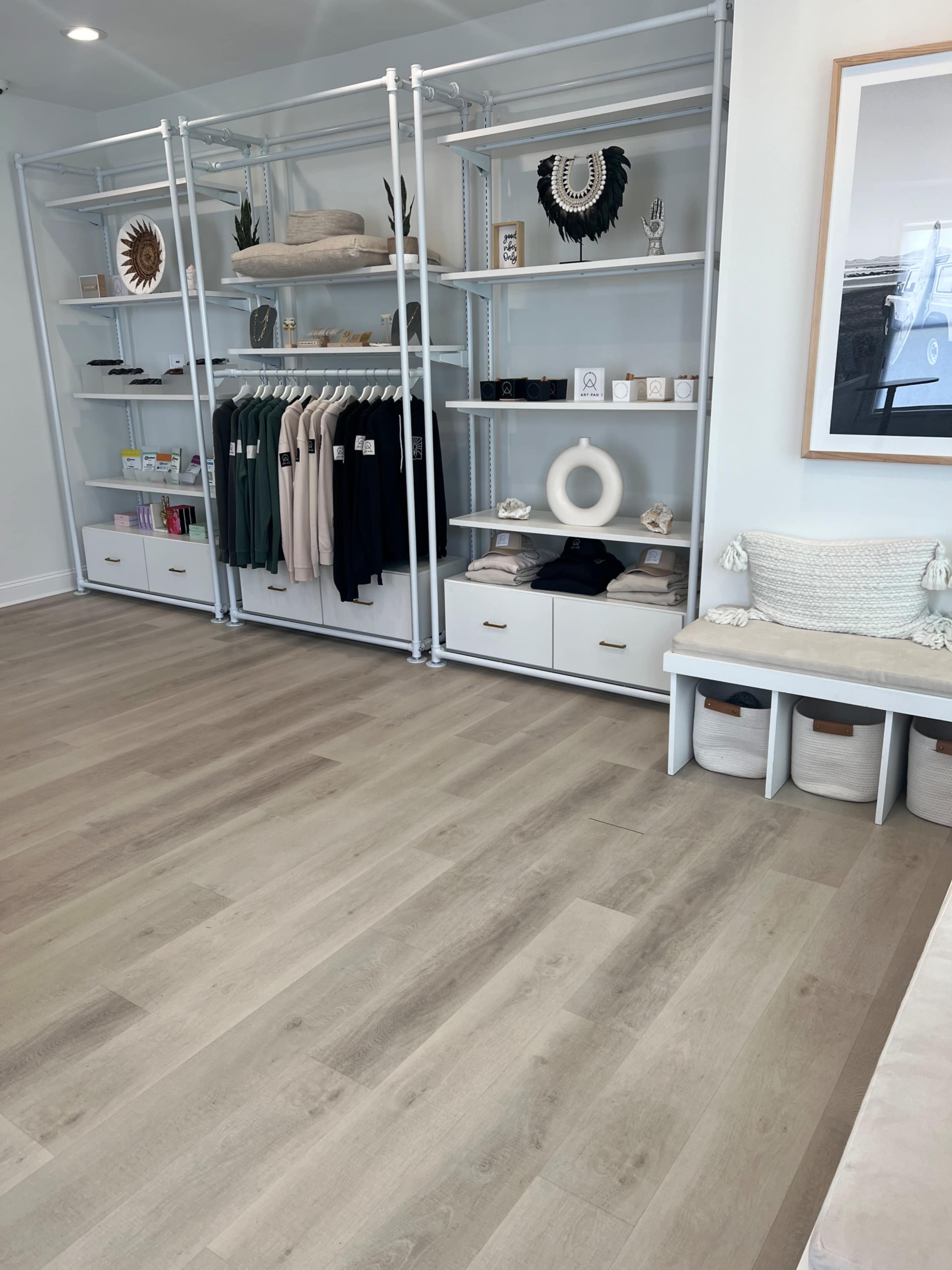 A modern retail space with neatly arranged shelves displaying clothing and accessories, alongside organized bins and a seating area.