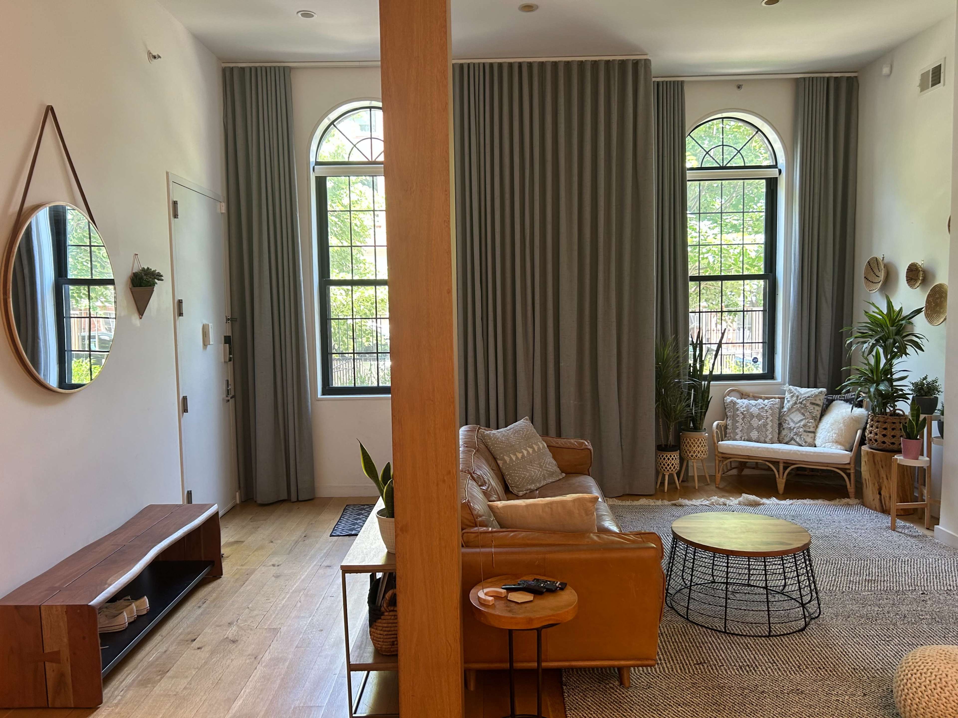 A welcoming living room with large windows, a beige sofa, a round coffee table, and decorative plants, divided by a wooden support beam.