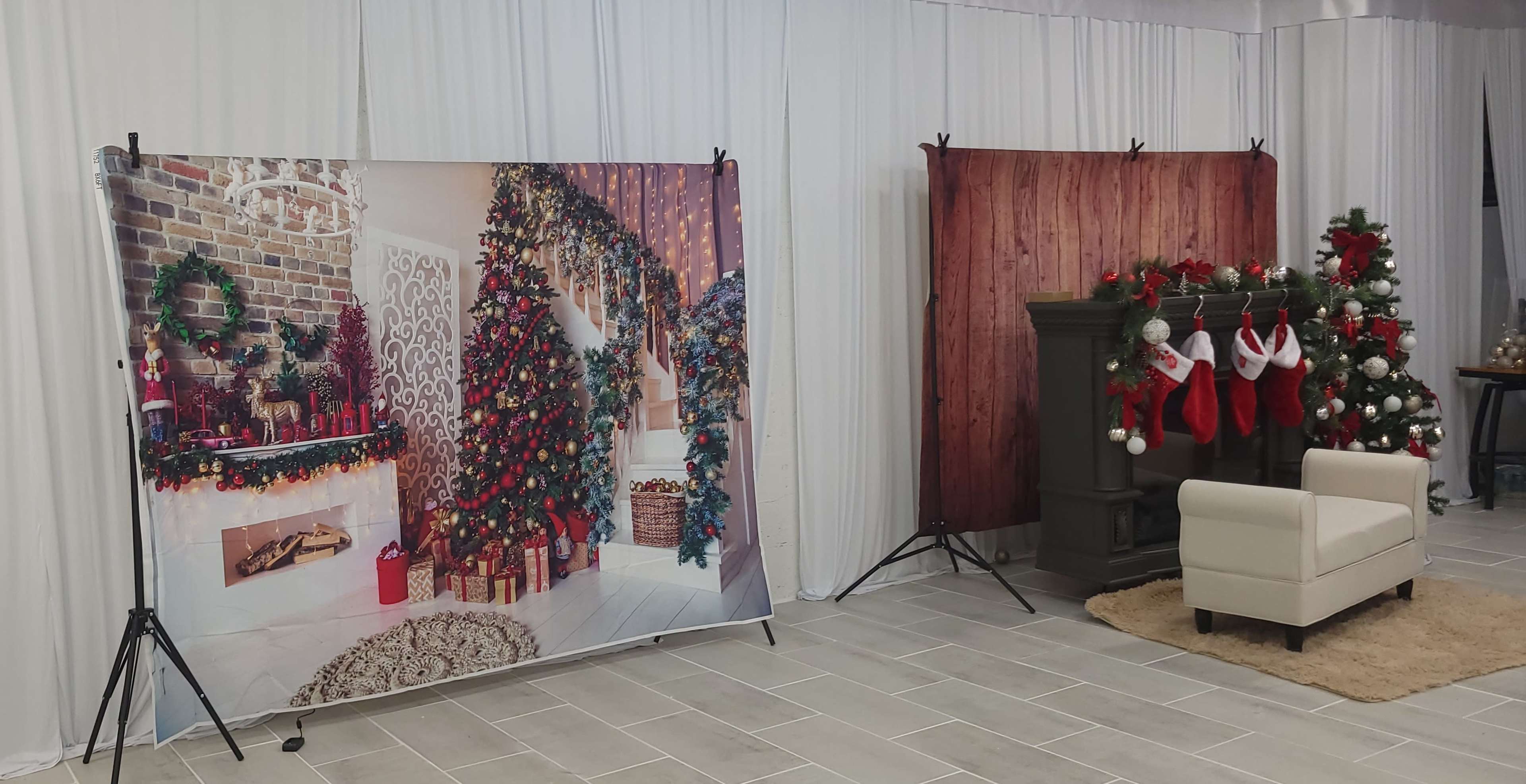 A decorated photo booth area with holiday-themed backdrops, including a festive room setting and a wooden wall, alongside a fireplace adorned with stockings and a Christmas tree.