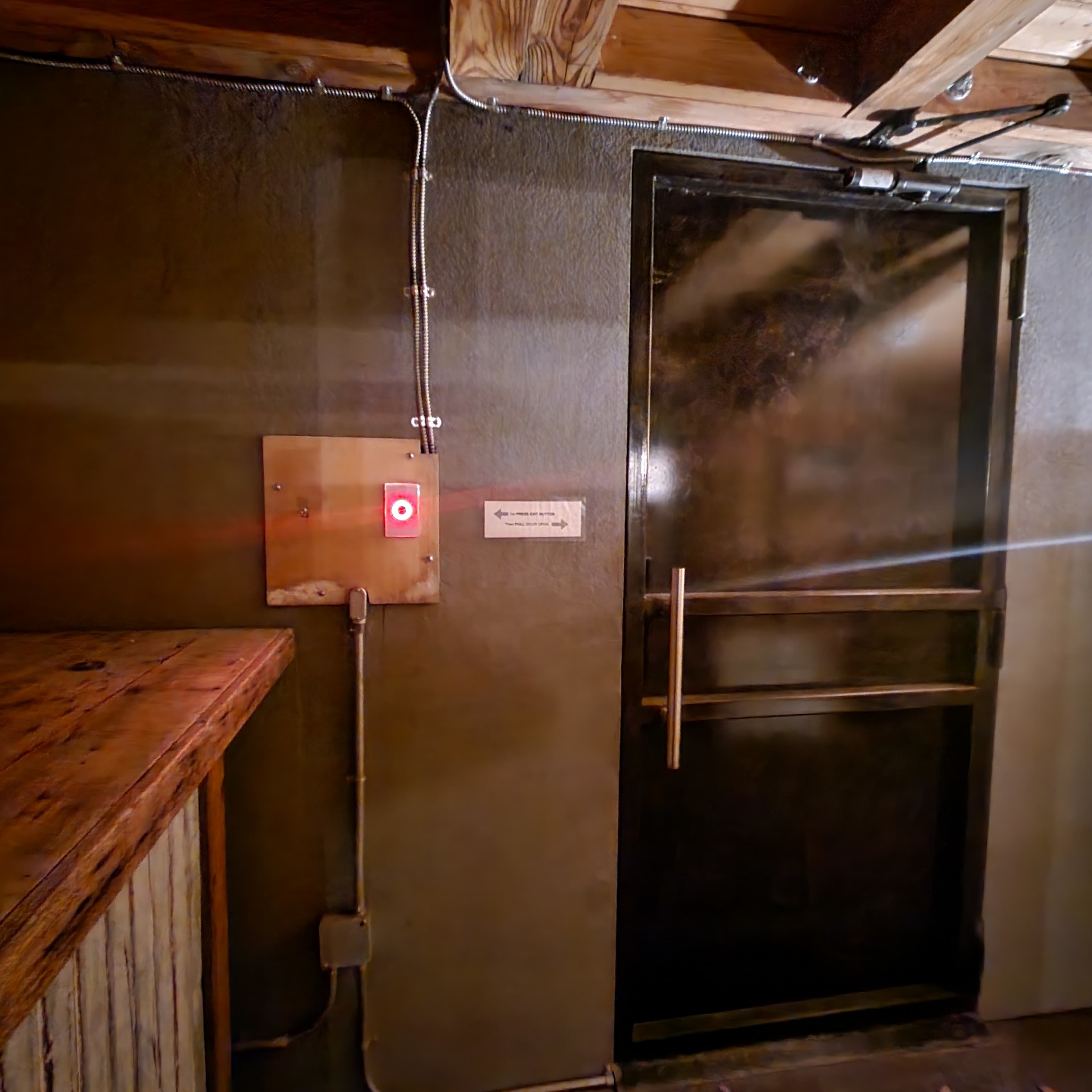 A dark hallway with a metallic door fitted with a red button on the wall beside it.