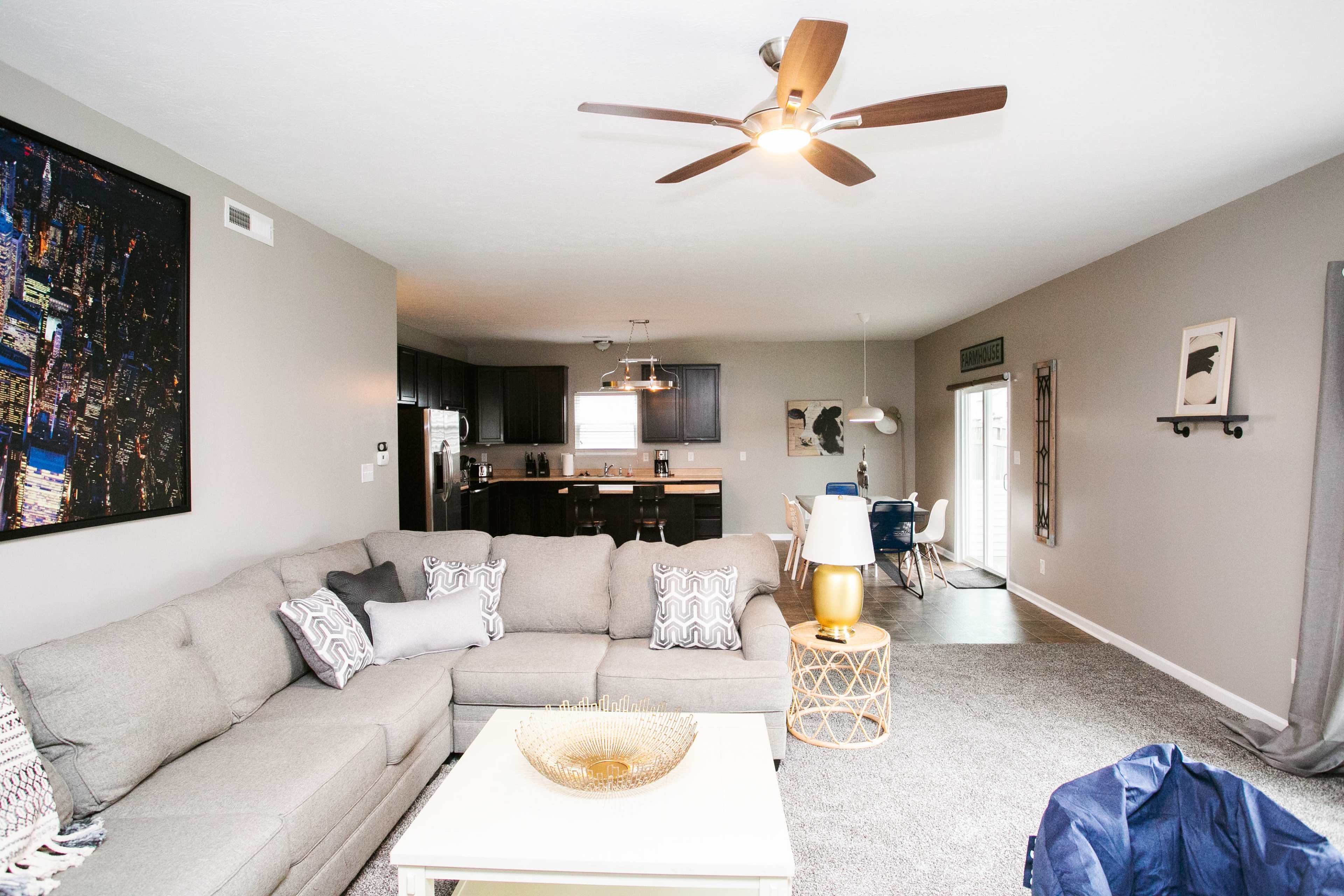 The living room features a large sectional sofa, a coffee table, and a view into an adjoining kitchen with dark cabinetry.
