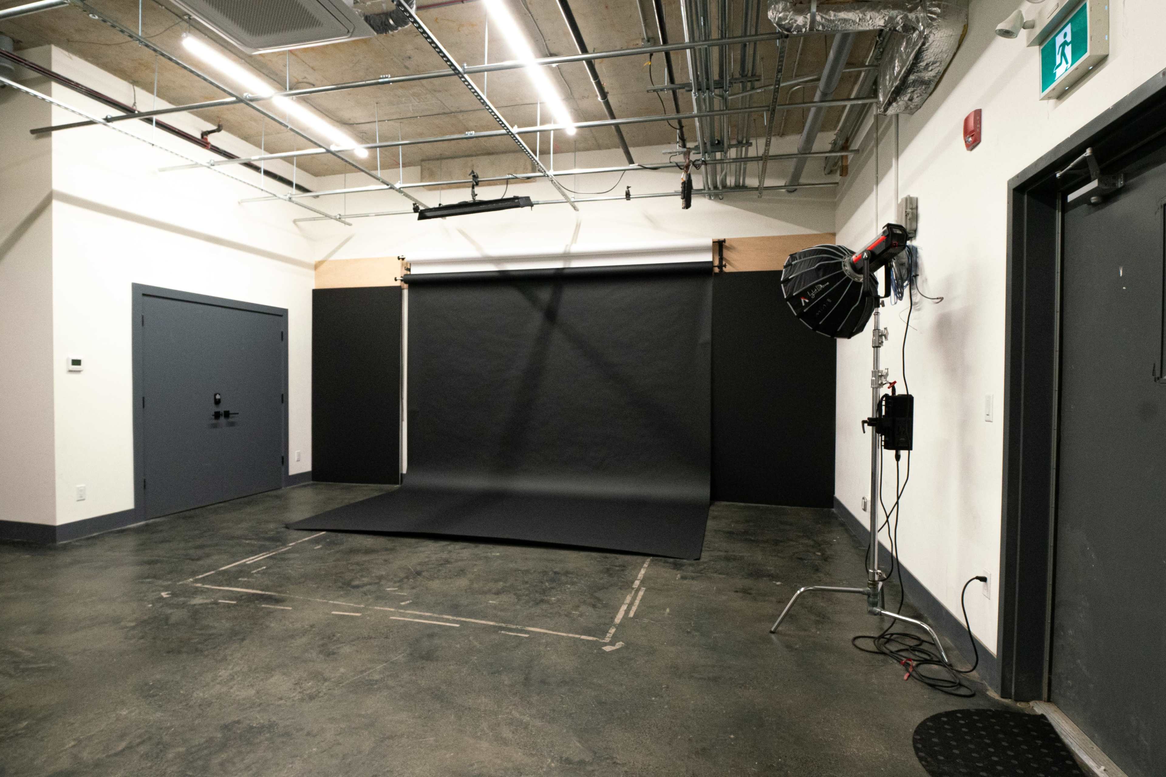 A photography studio with a black backdrop, a lighting setup, and a smooth concrete floor.