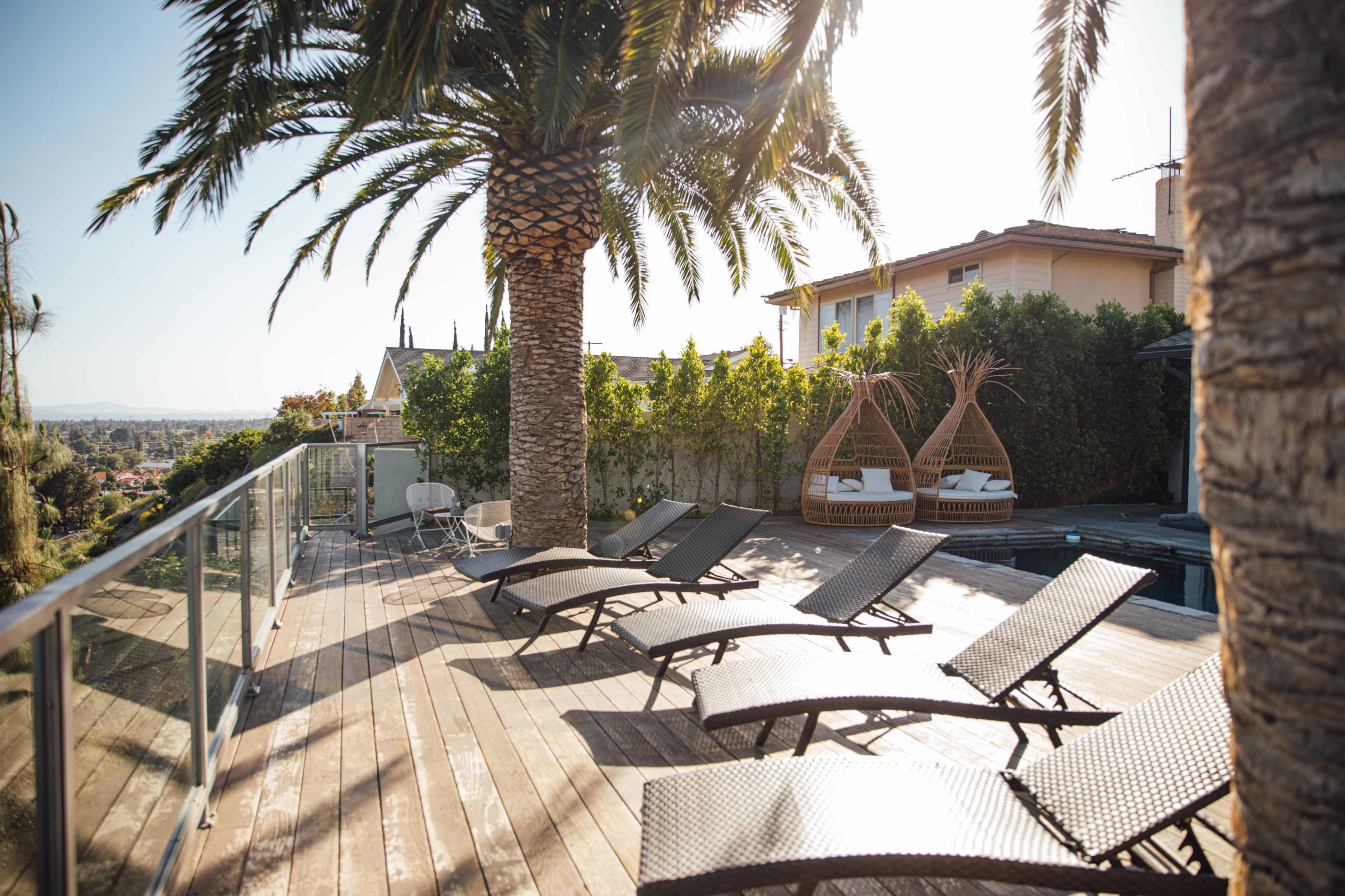 A deck with loungers and two hanging chairs overlooks a landscaped area with palm trees.