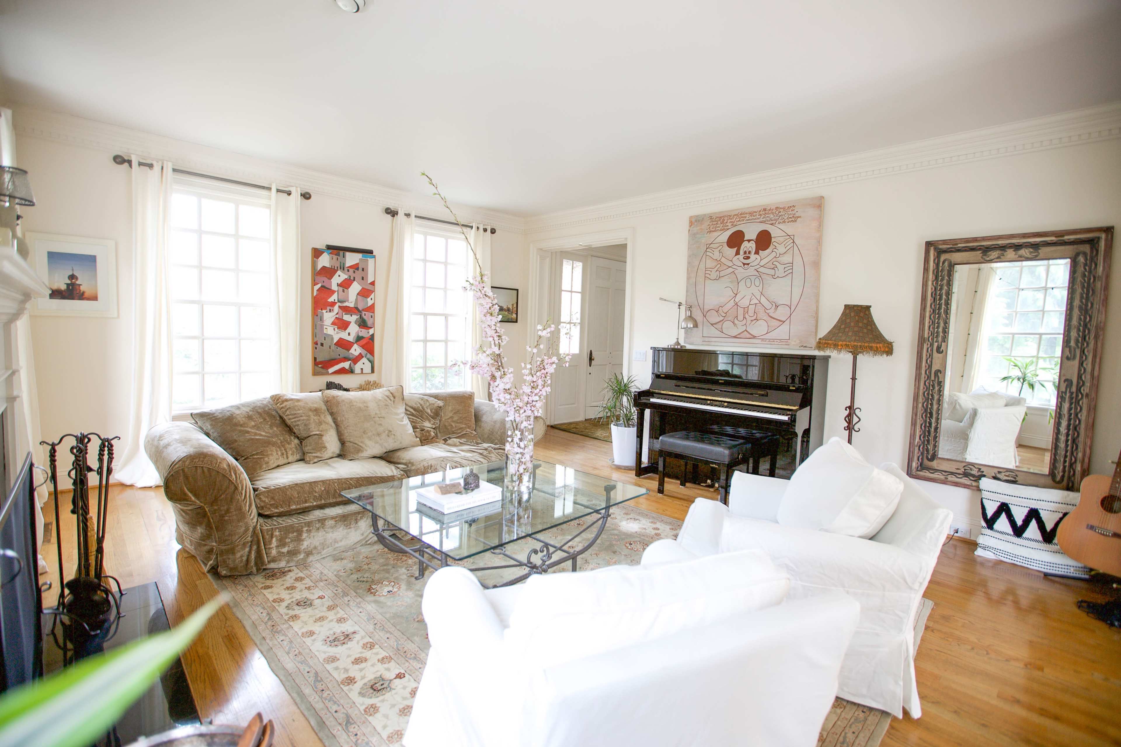 A spacious living room features a plush sofa, a glass coffee table, a grand piano, and large windows allowing natural light to fill the space.