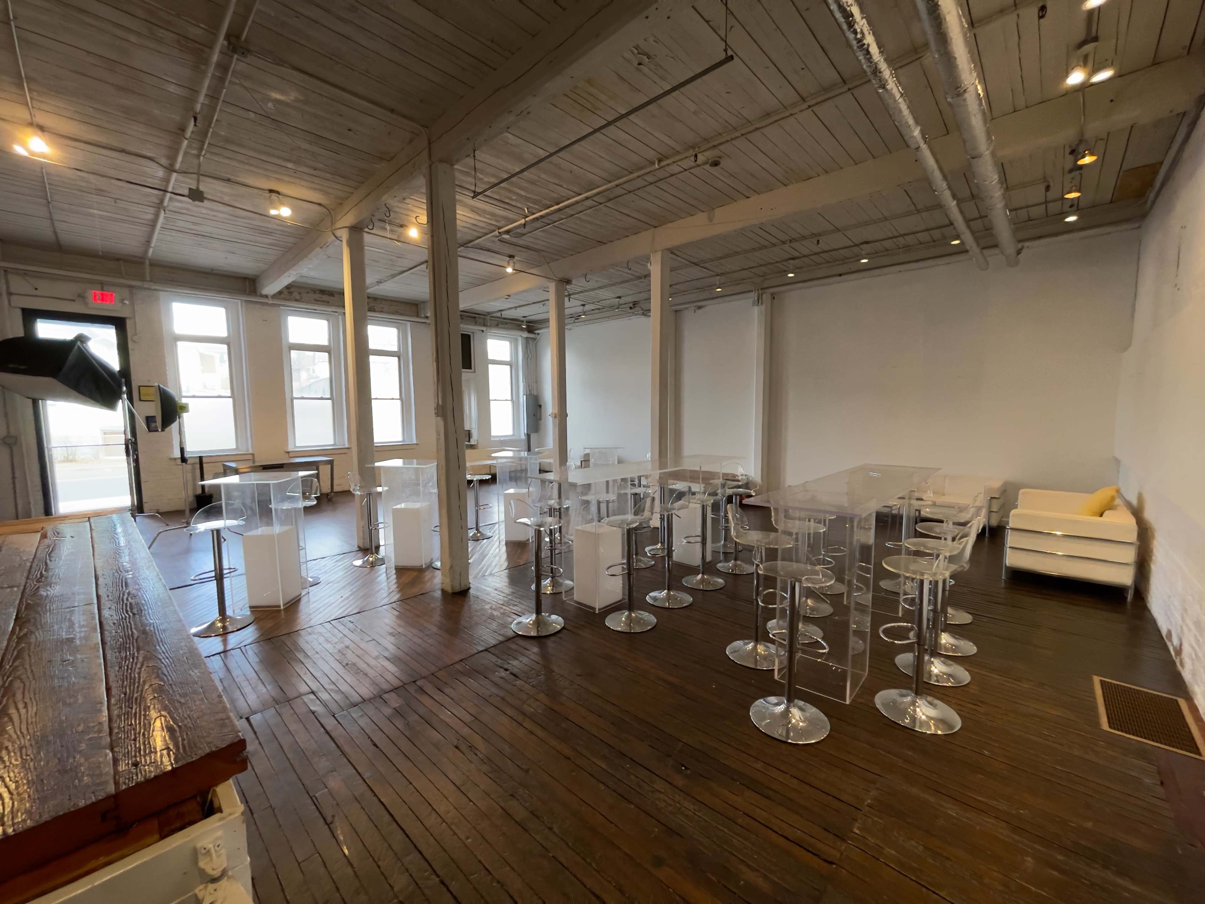 A spacious, well-lit interior of a modern venue with clear tables and stools arranged neatly on a wooden floor.