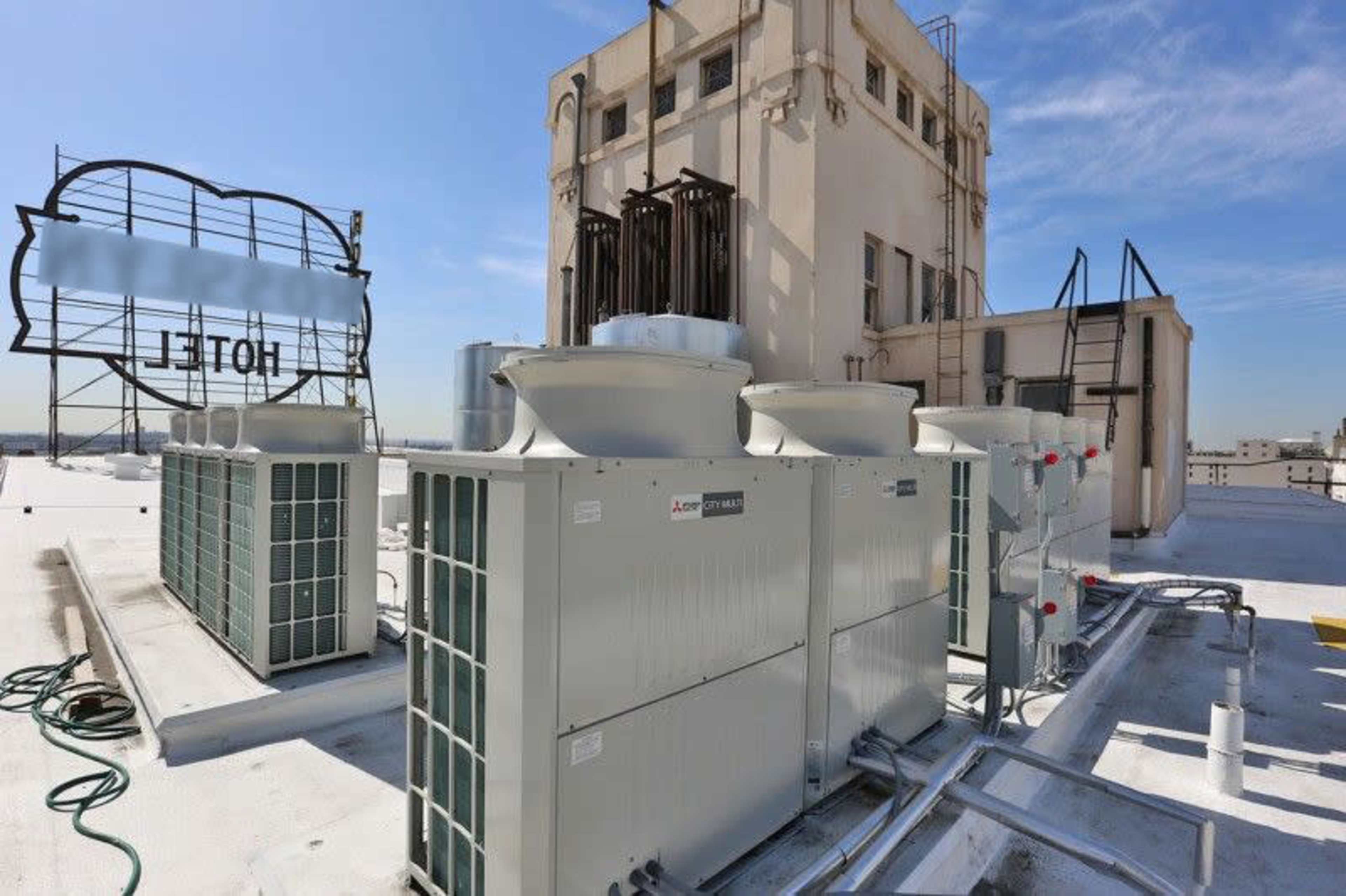 Rooftop HVAC units and cooling equipment on a building, with the city skyline visible in the background.