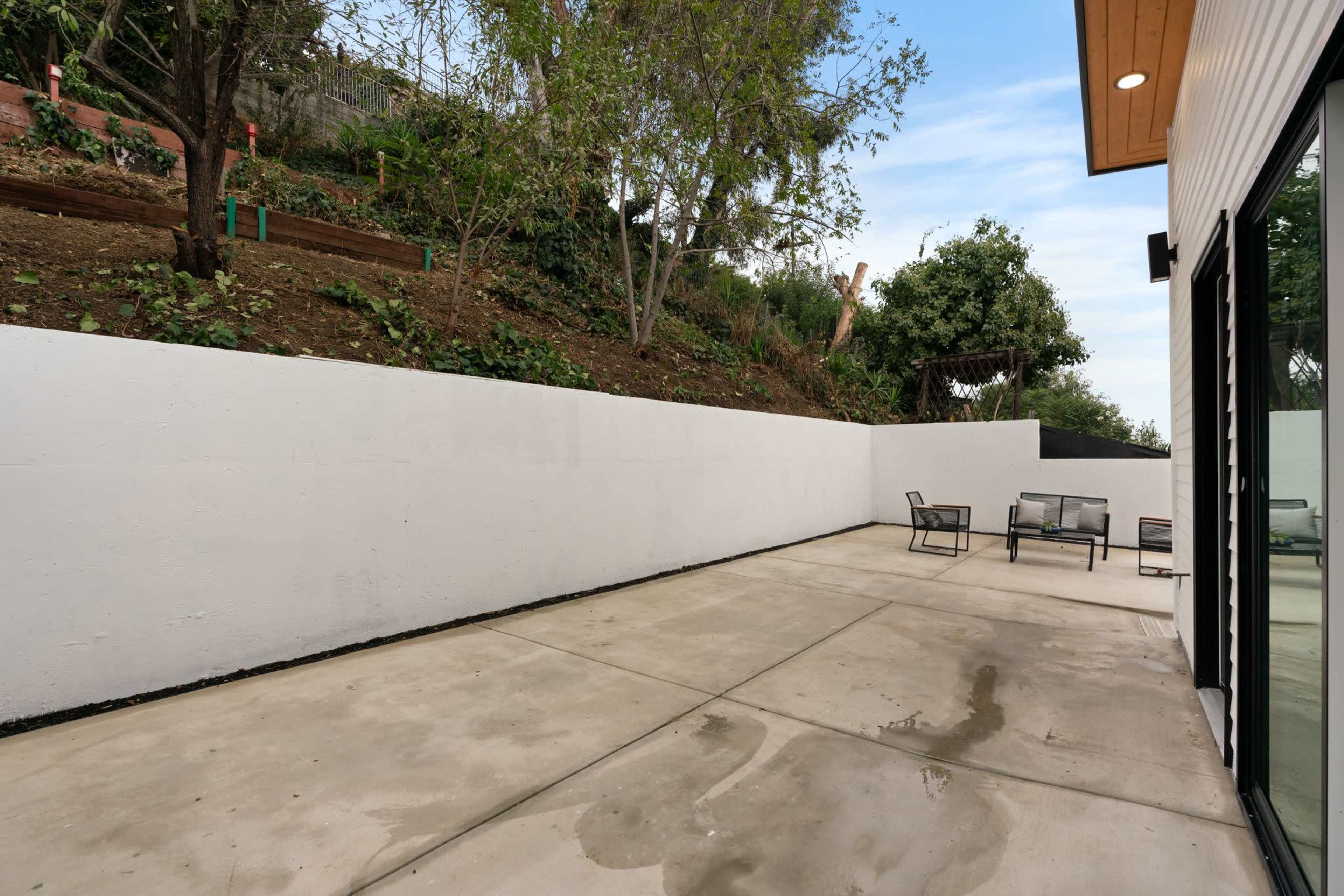 The image shows a concrete patio area surrounded by a sloped garden with sparse vegetation.