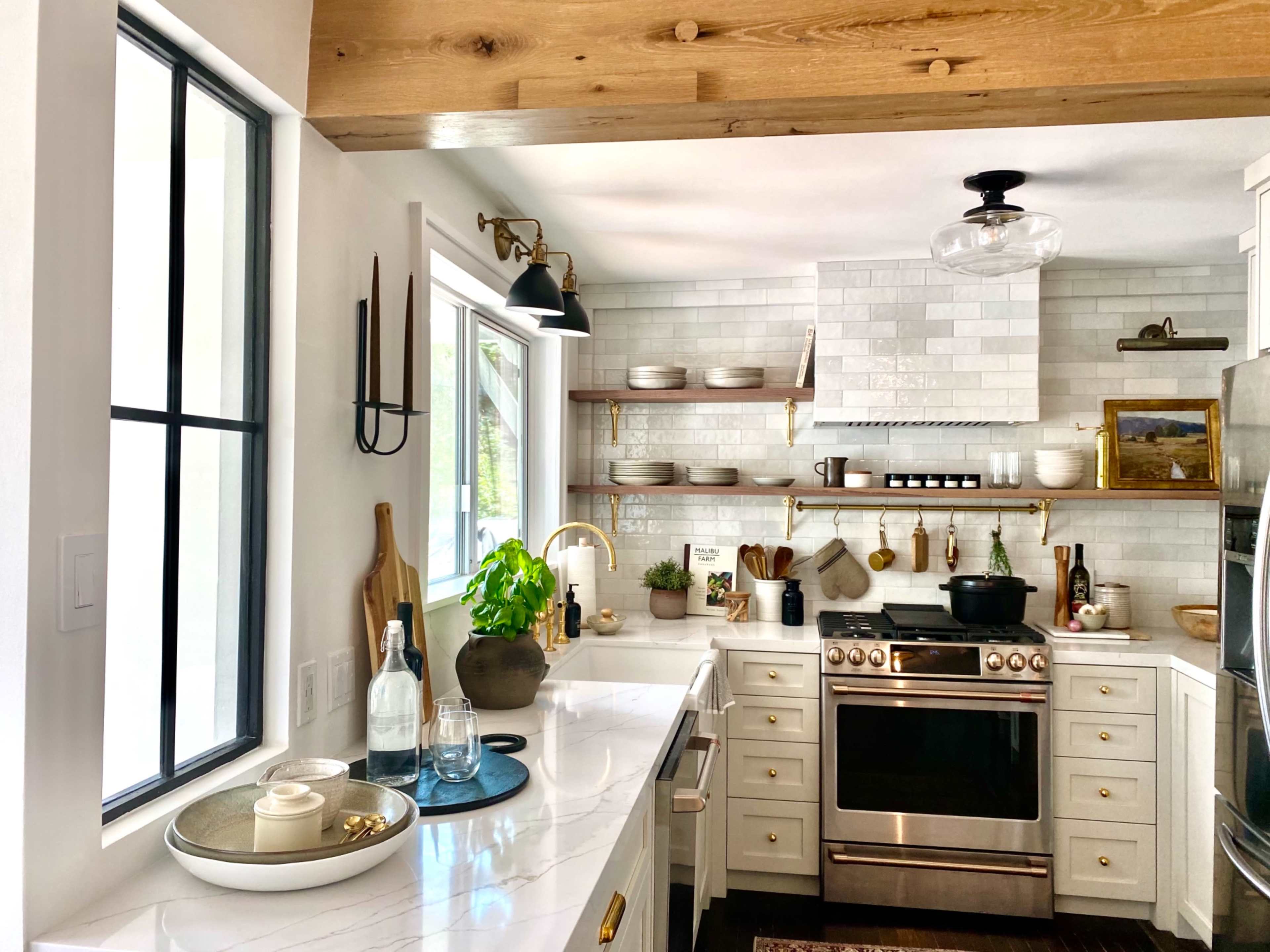 A modern kitchen features white cabinetry, a stone backsplash, and stainless steel appliances, with natural light streaming in through large windows.