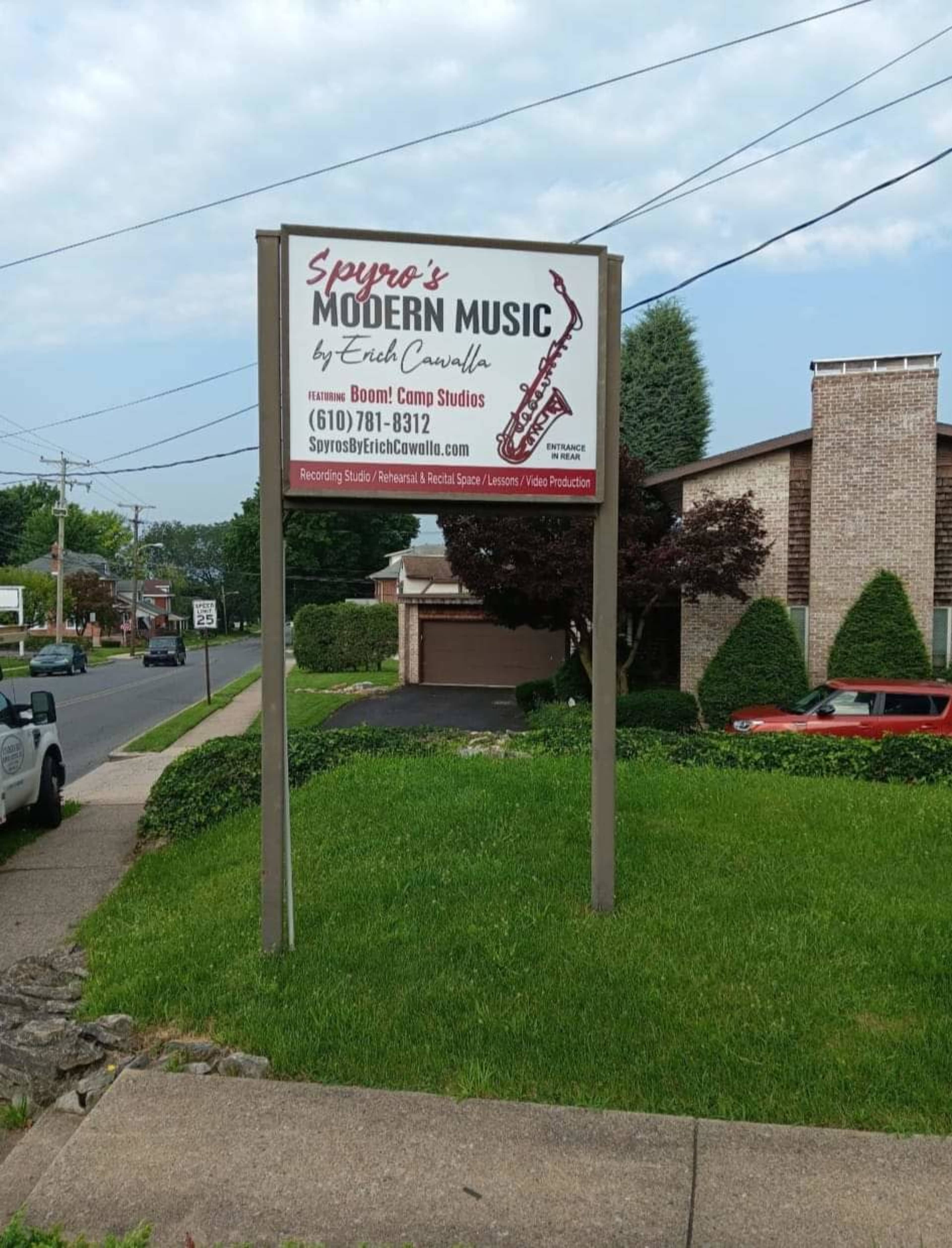 A large sign for Spyros Modern Music is situated near the roadside, providing contact information and indicating the location of a recording studio.