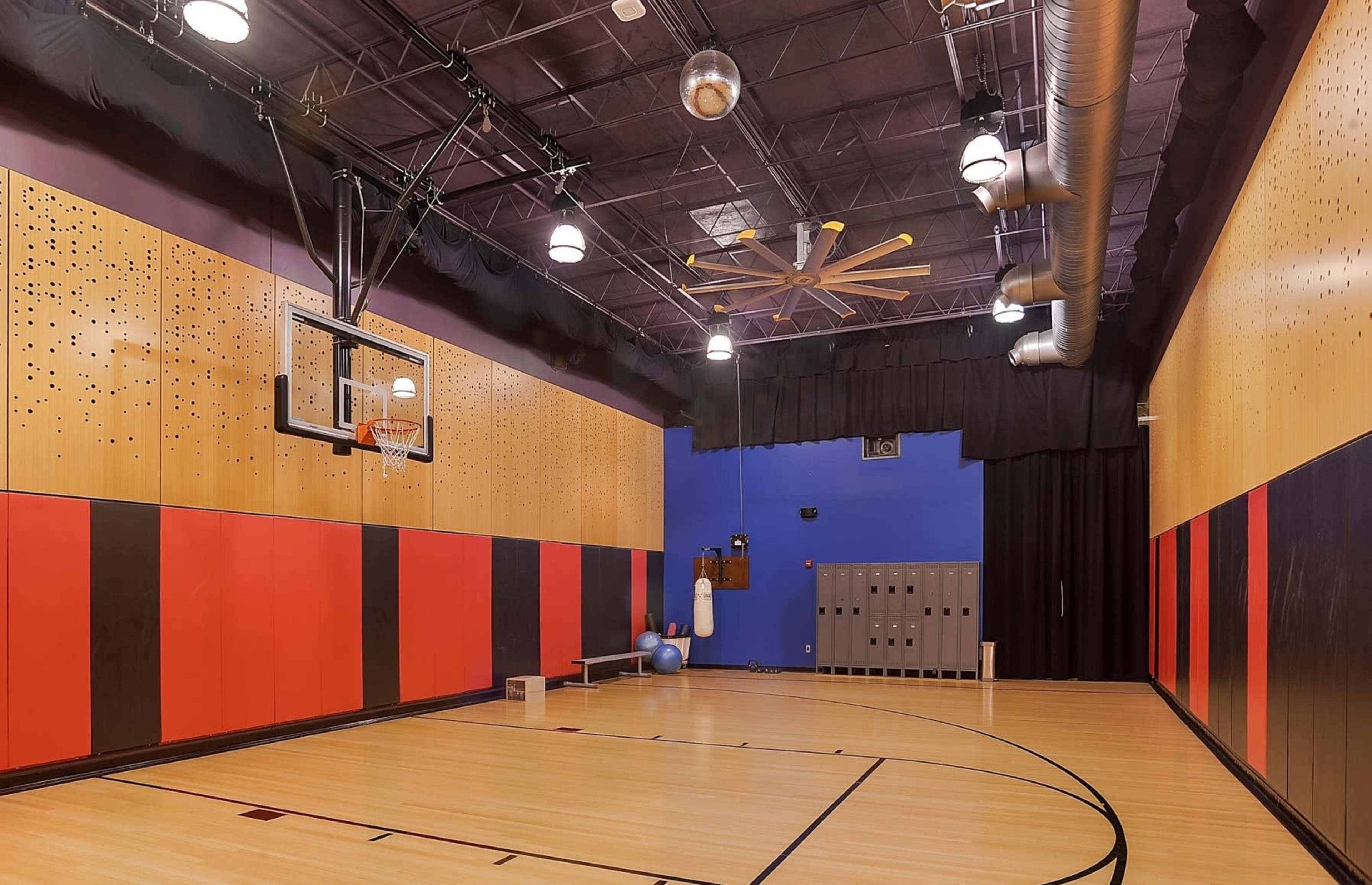 An indoor basketball court featuring a hoop, a wooden floor, and colorful wall panels.
