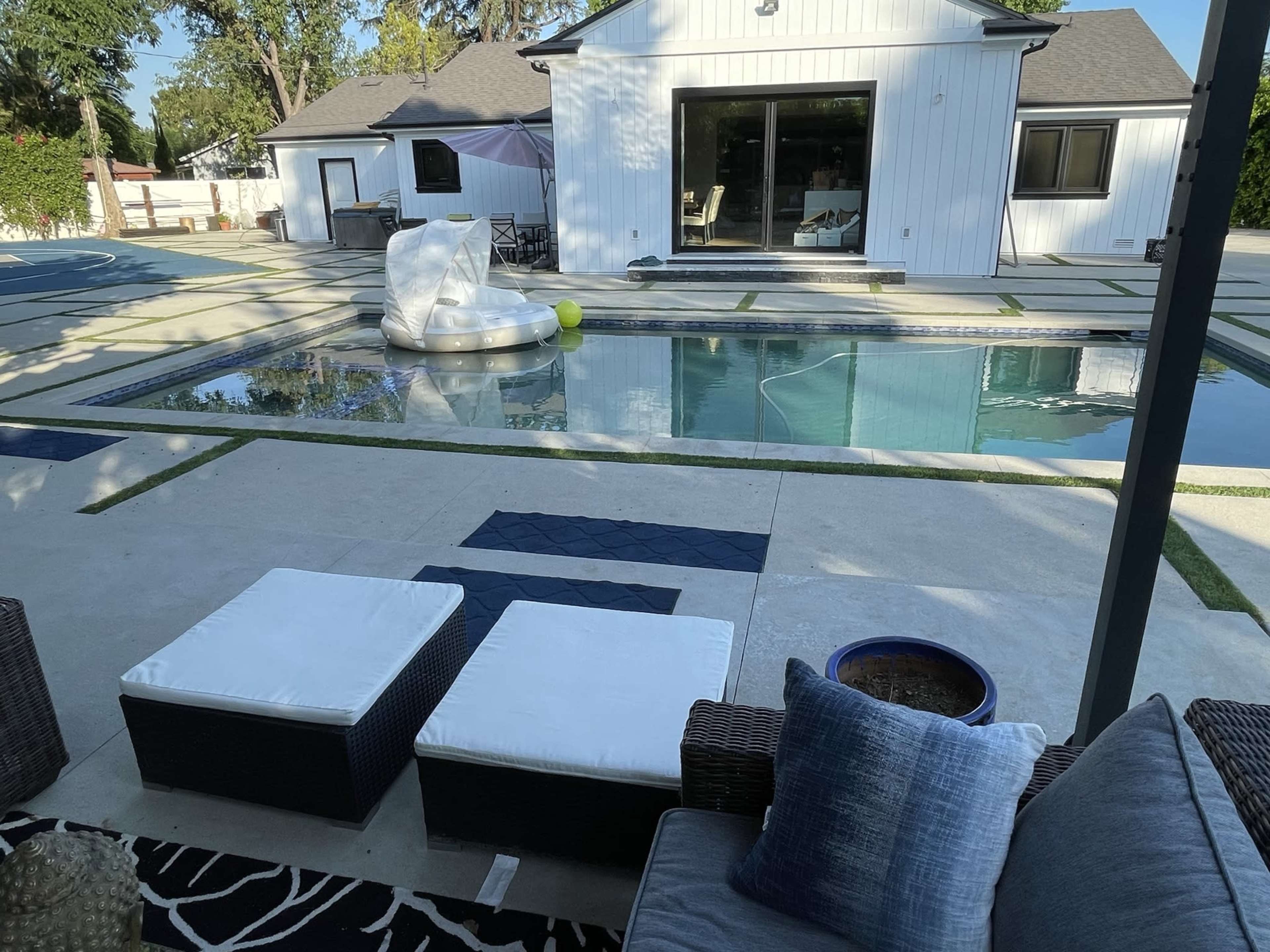 A clean outdoor area with a swimming pool, loungers, and a modern house in the background.