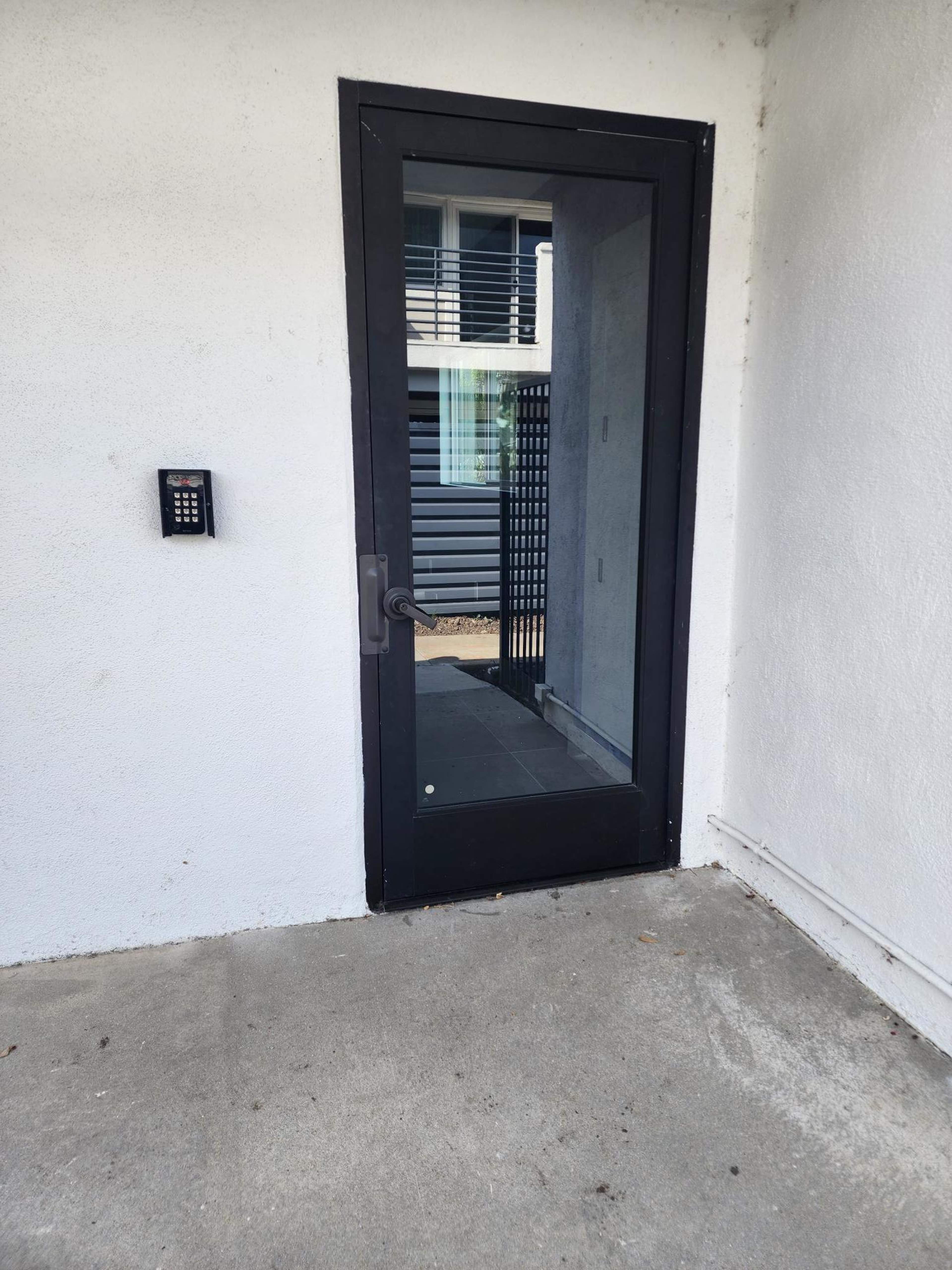 A black glass door with a keypad on the left side, situated against a white wall.