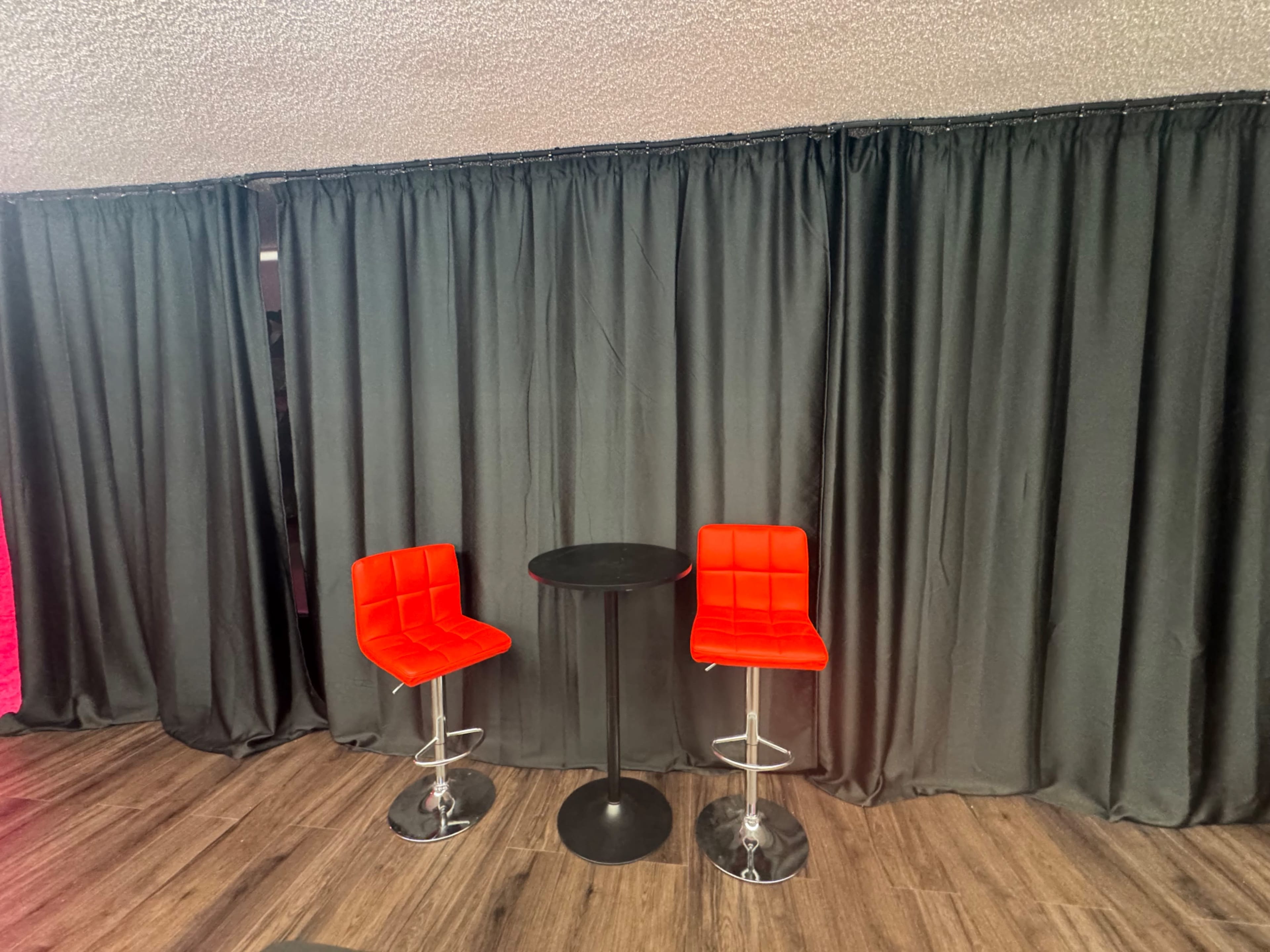 Two red bar stools are positioned next to a small black table in front of a black curtain backdrop.