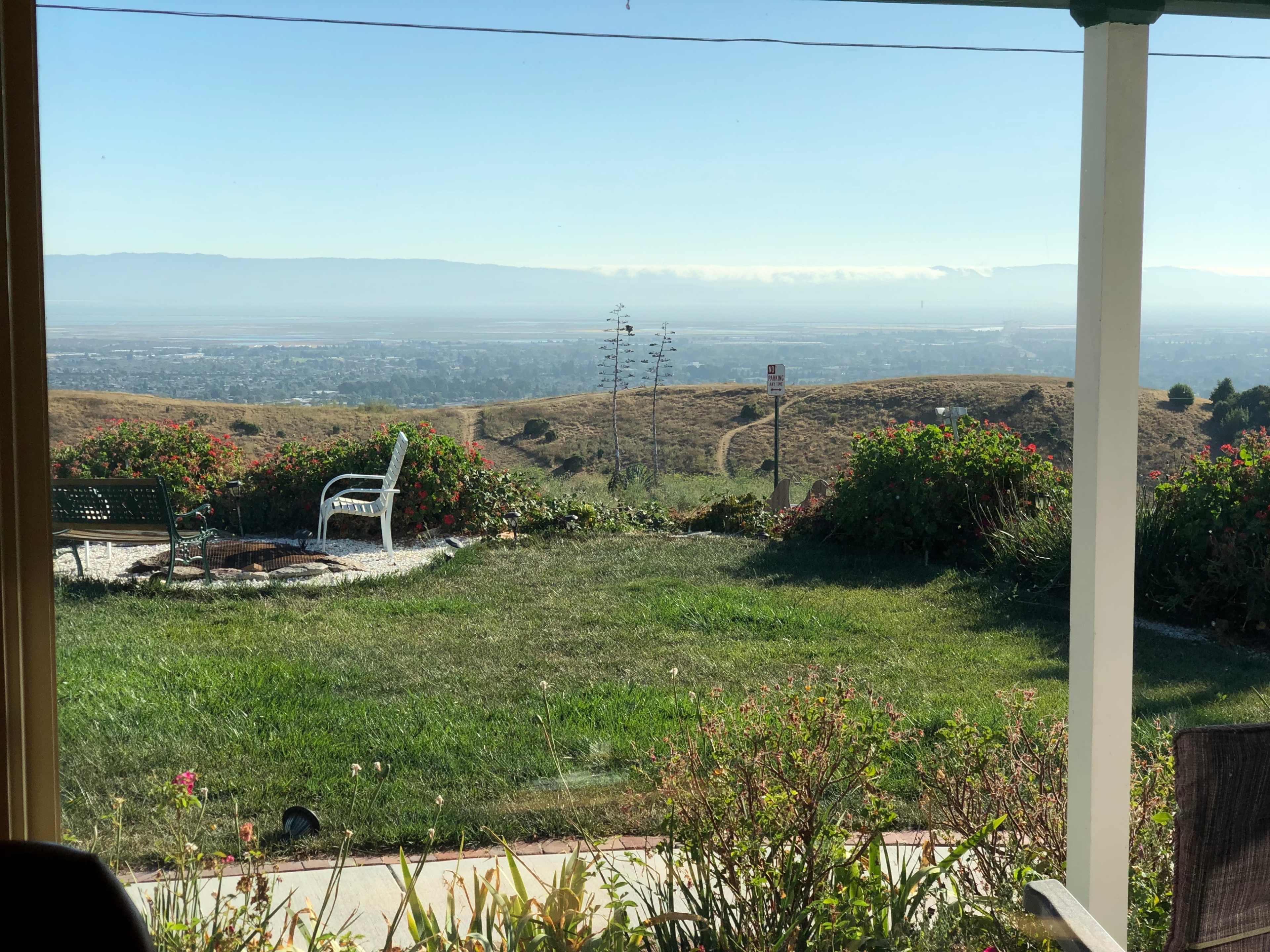 A view from a porch overlooking a grassy landscape that slopes down to a valley with distant hills in the background.