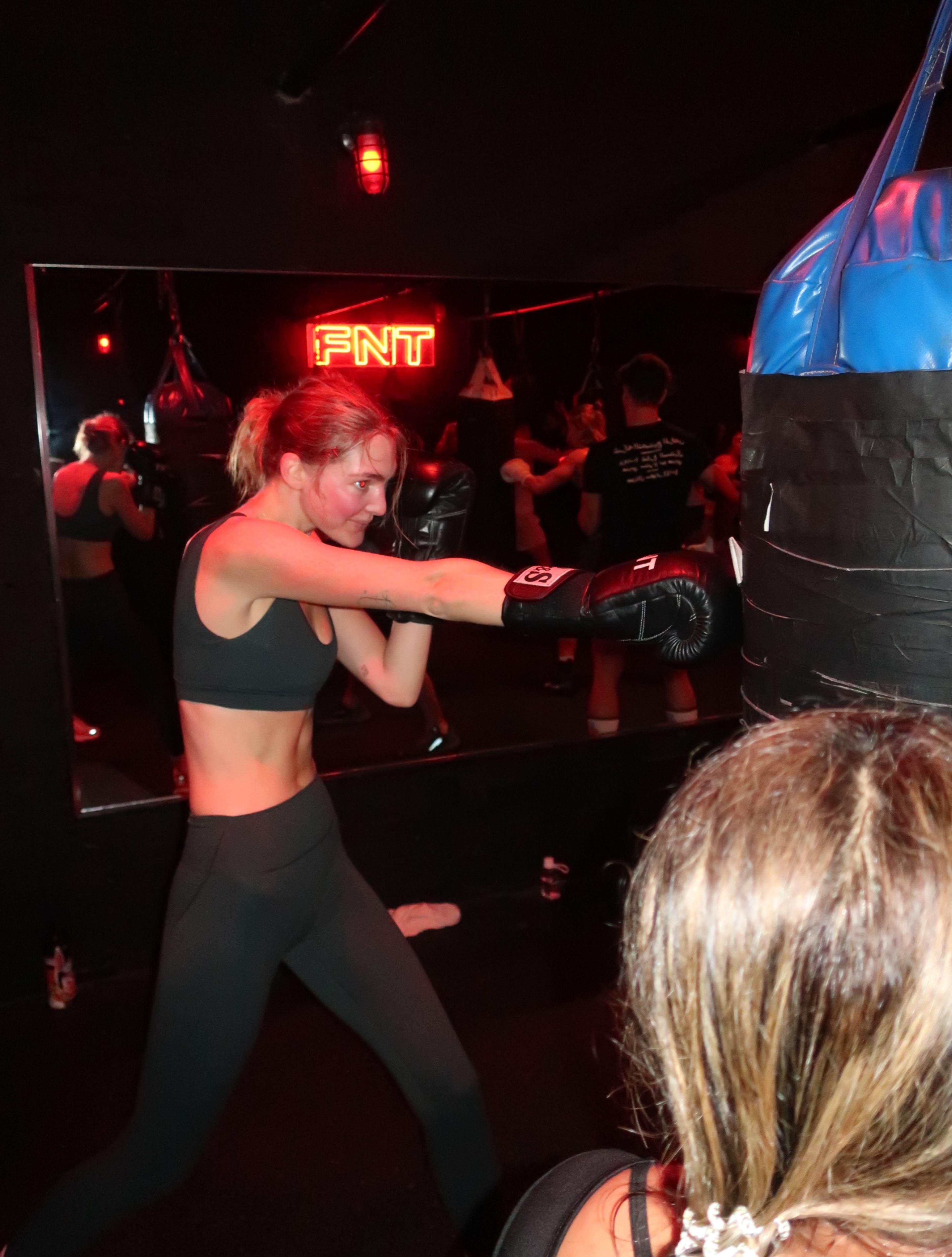 A woman in athletic attire is throwing a punch at a boxing bag in a dimly lit gym.