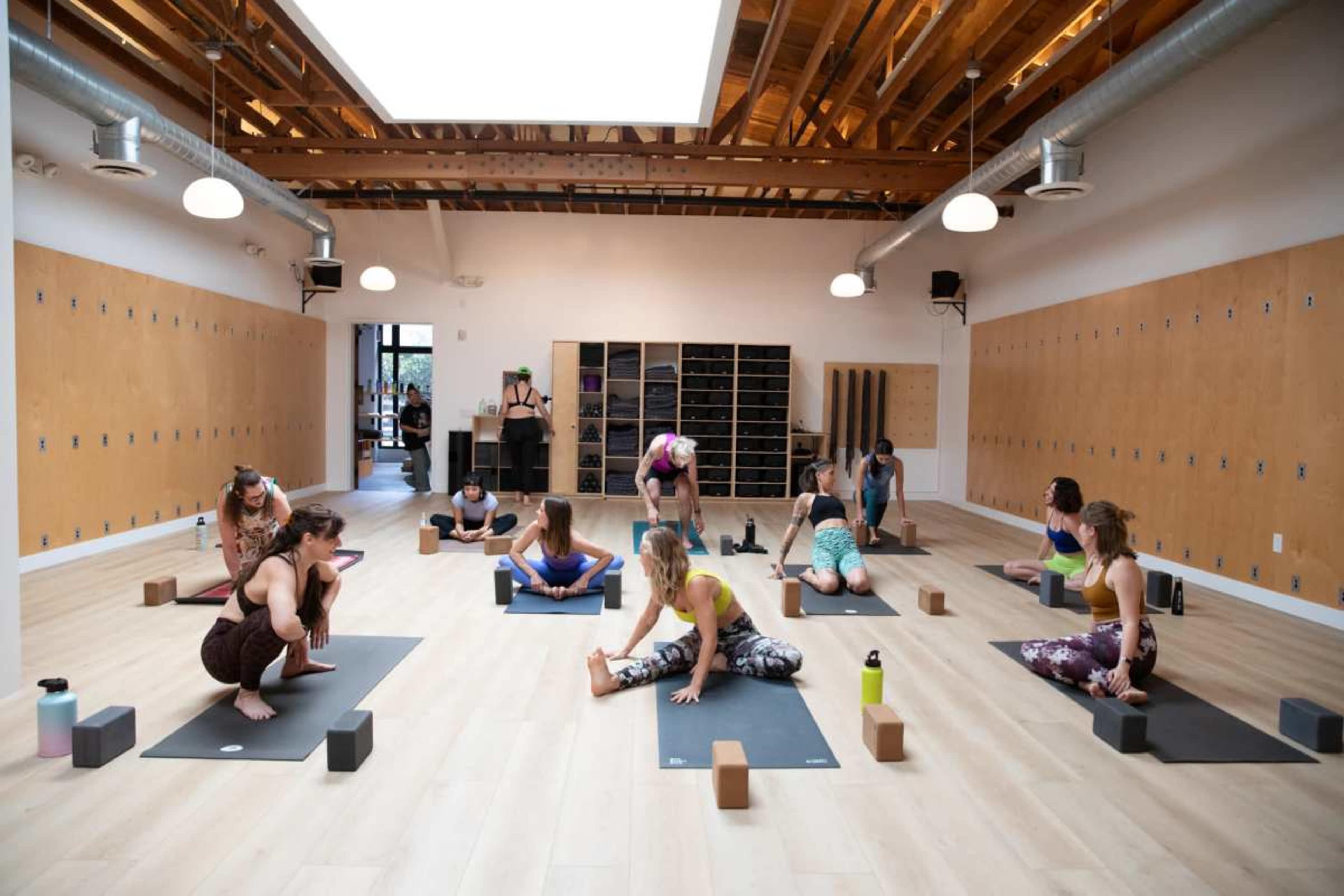 A group of people is practicing yoga in a spacious studio with wooden flooring and natural light.