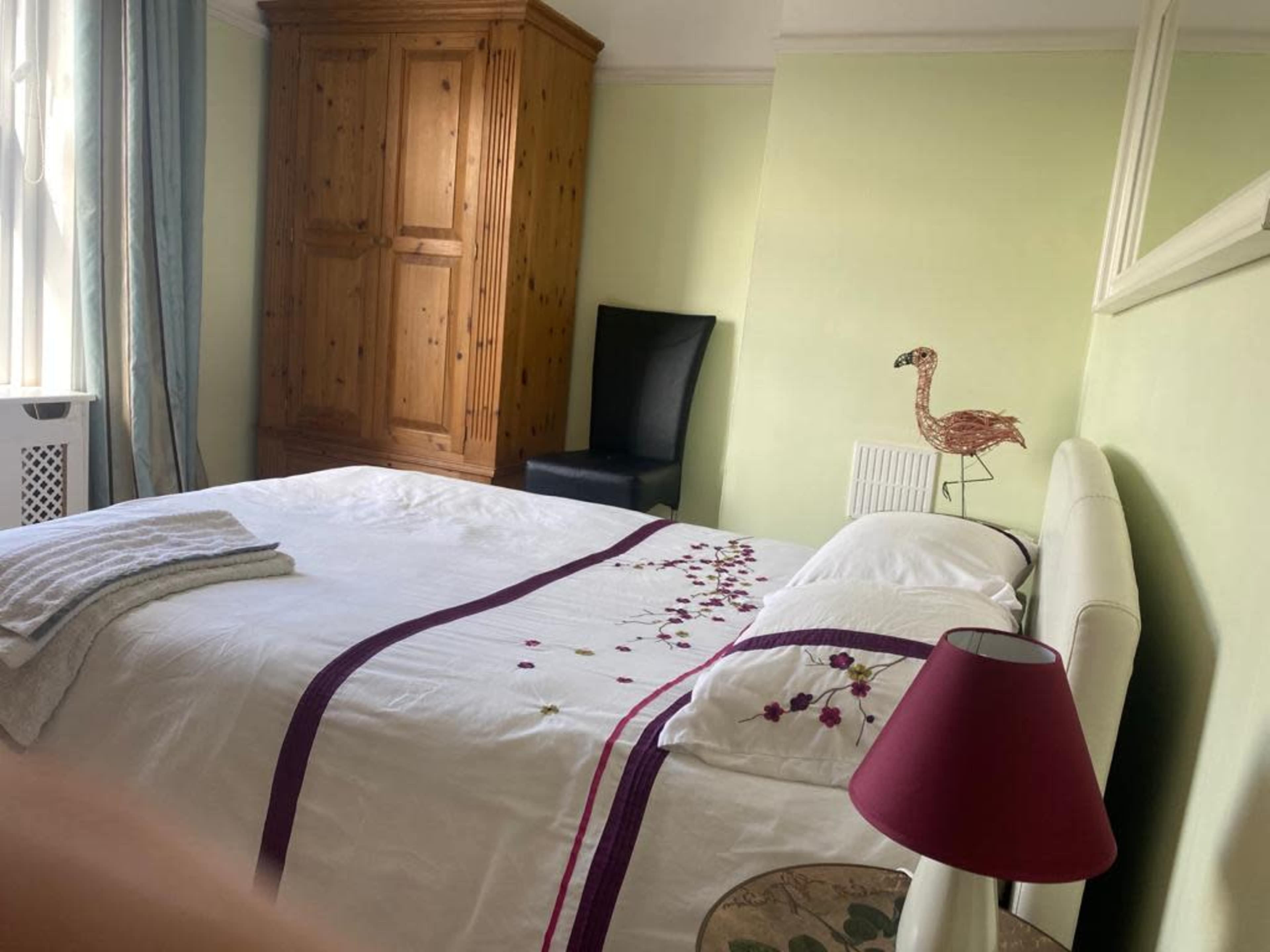 A bedroom with a white bed adorned with floral embroidery, a wooden wardrobe, a black chair, and a red lamp.