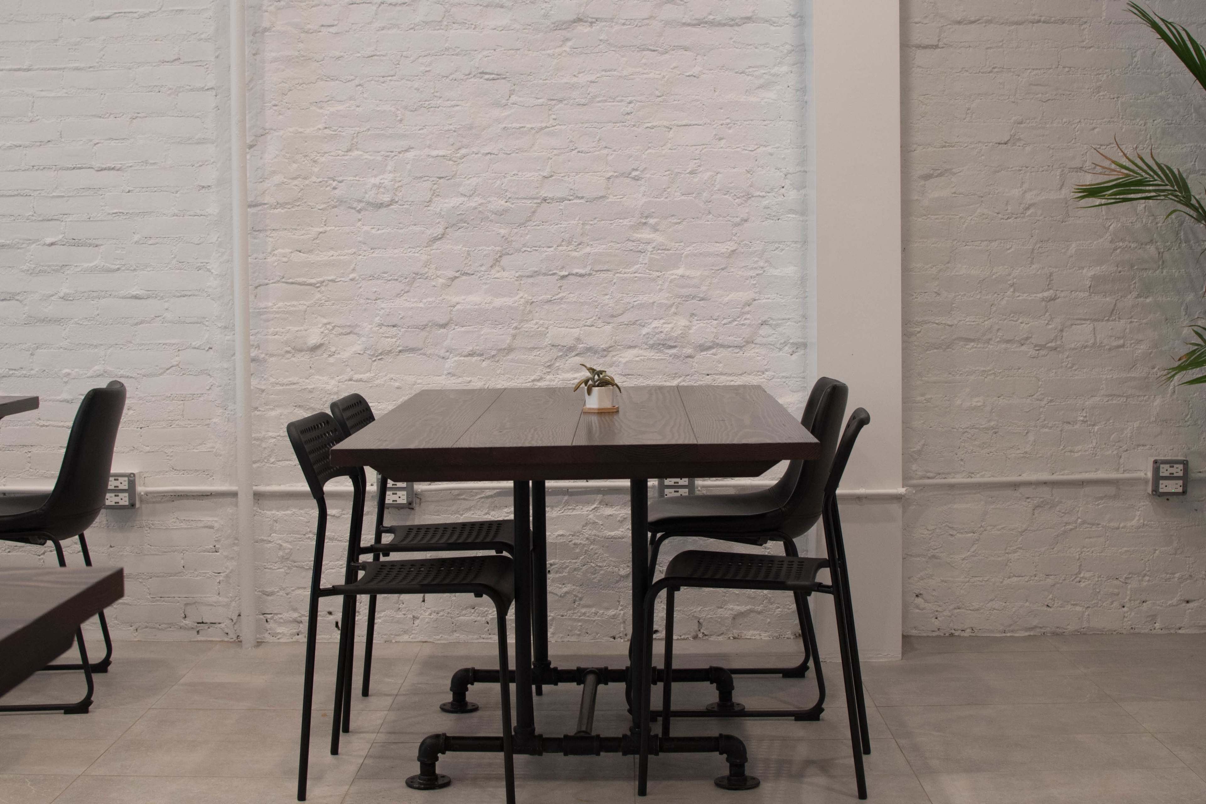 A simple table with chairs is positioned against a white brick wall, with a small plant on the table.