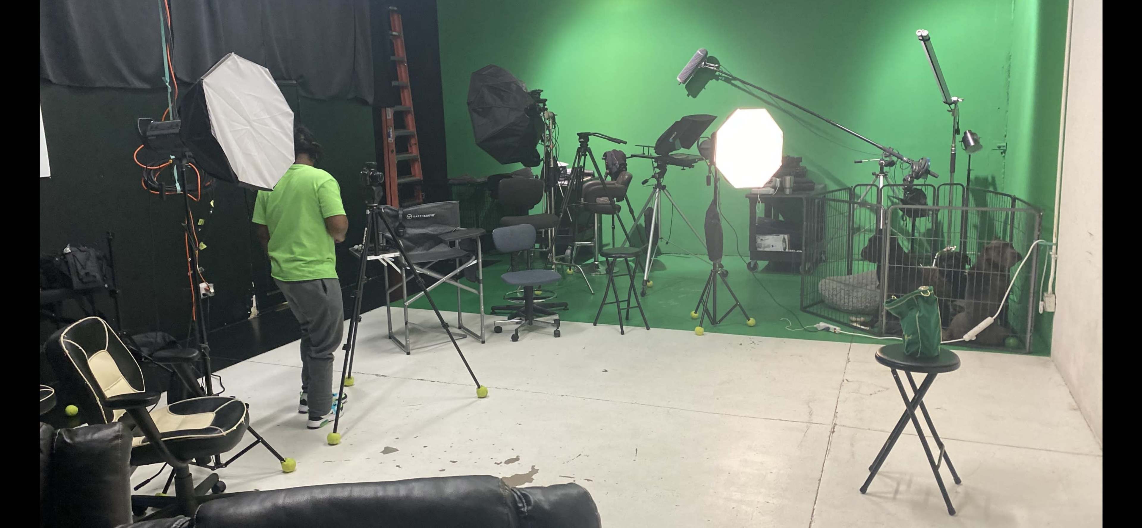 A person stands in a studio with a green backdrop, surrounded by various photography equipment, including lights and tripods.